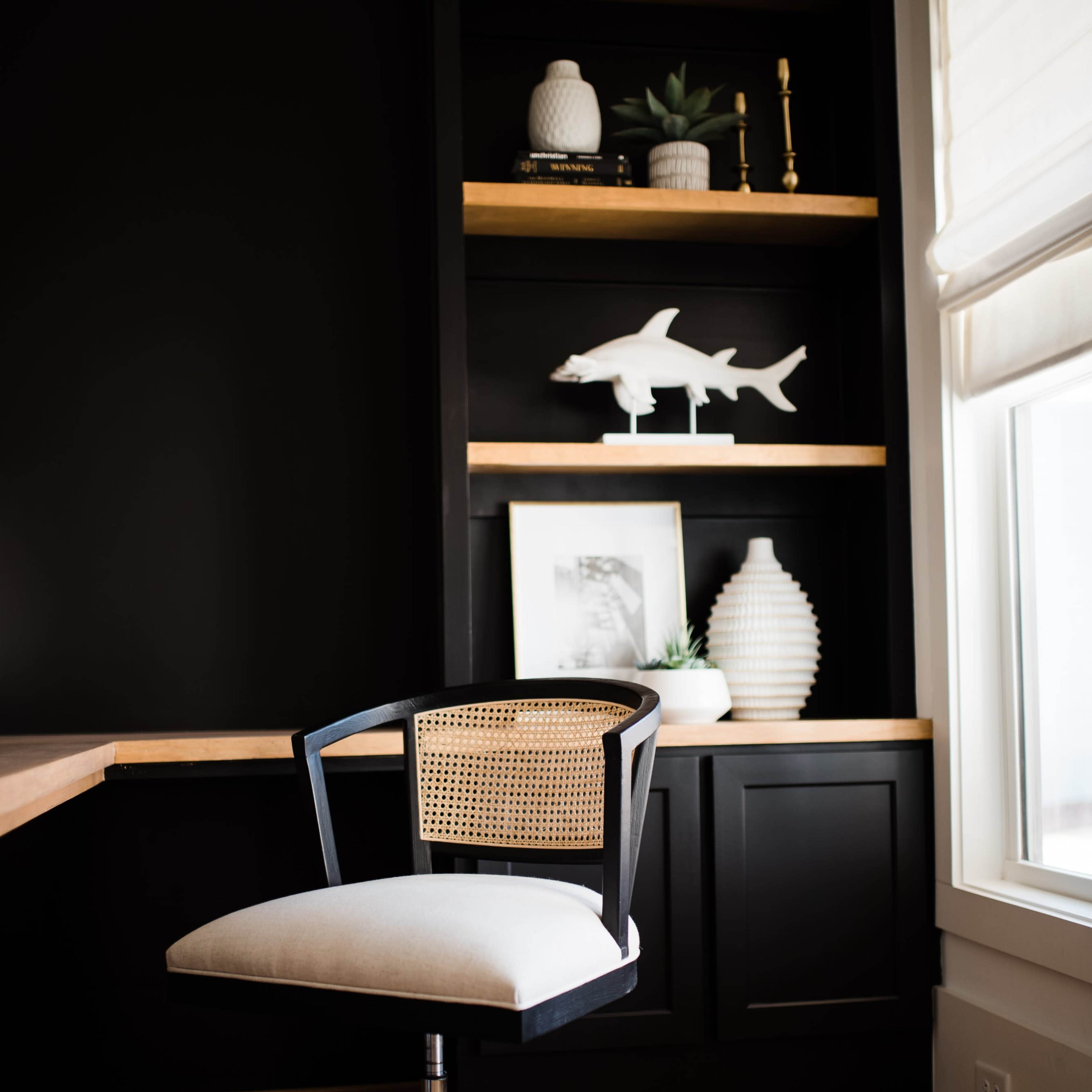 A modern office corner features a swivel chair in front of a dark shelf adorned with decorative items and plants.