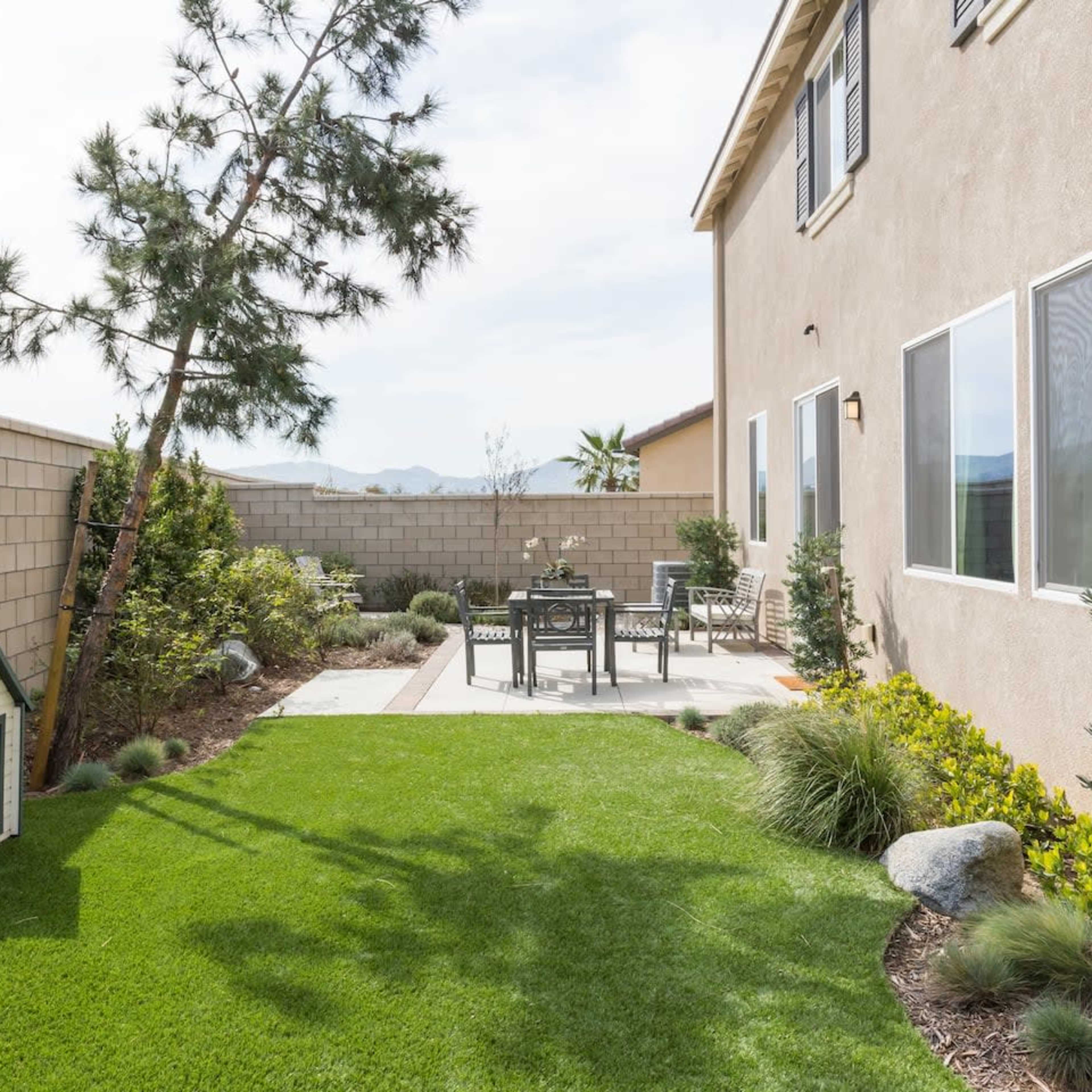 A well-maintained backyard featuring a small doghouse, a patio set with chairs, and landscaped greenery.