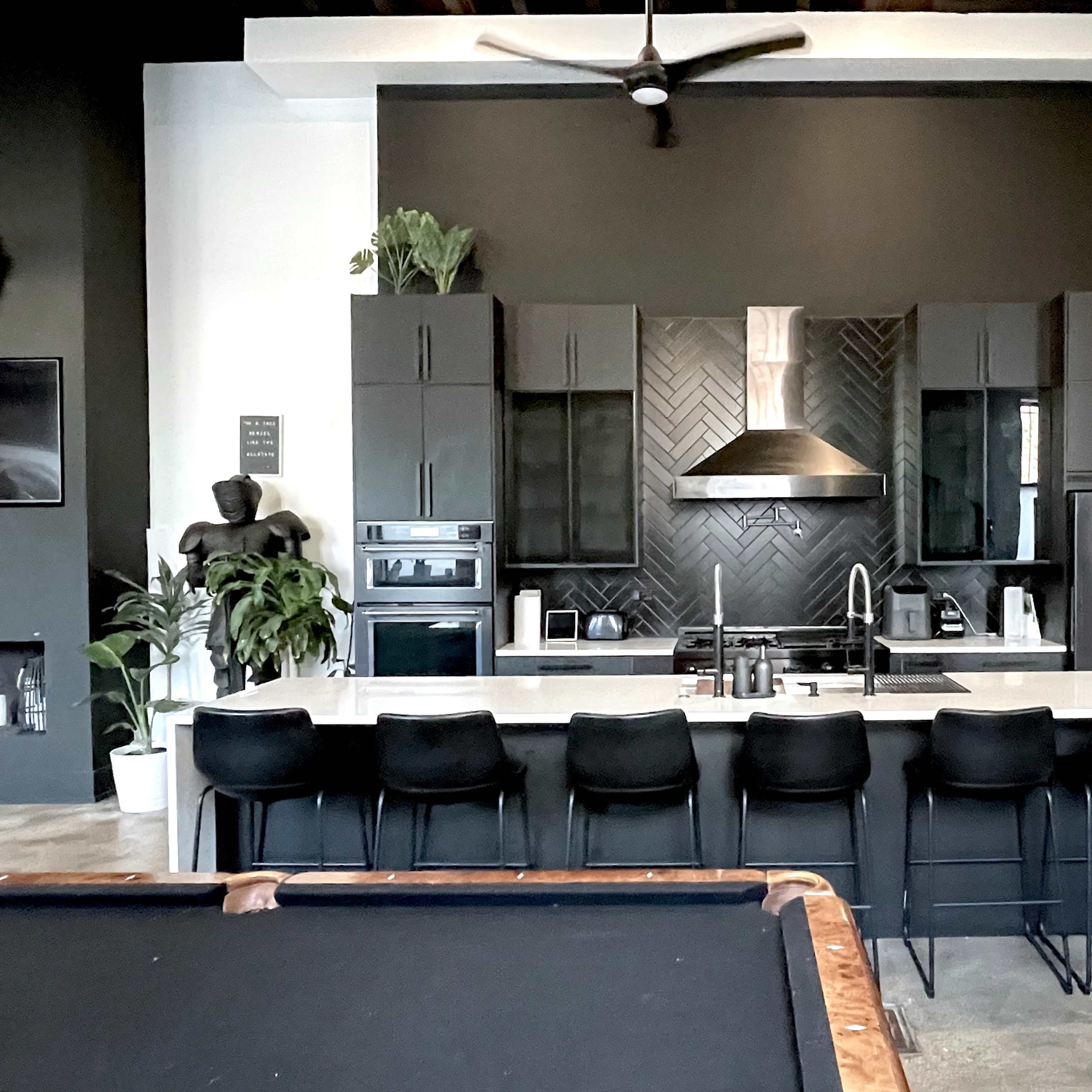A modern kitchen with black cabinetry, a white countertop, and a large island with several black bar stools.