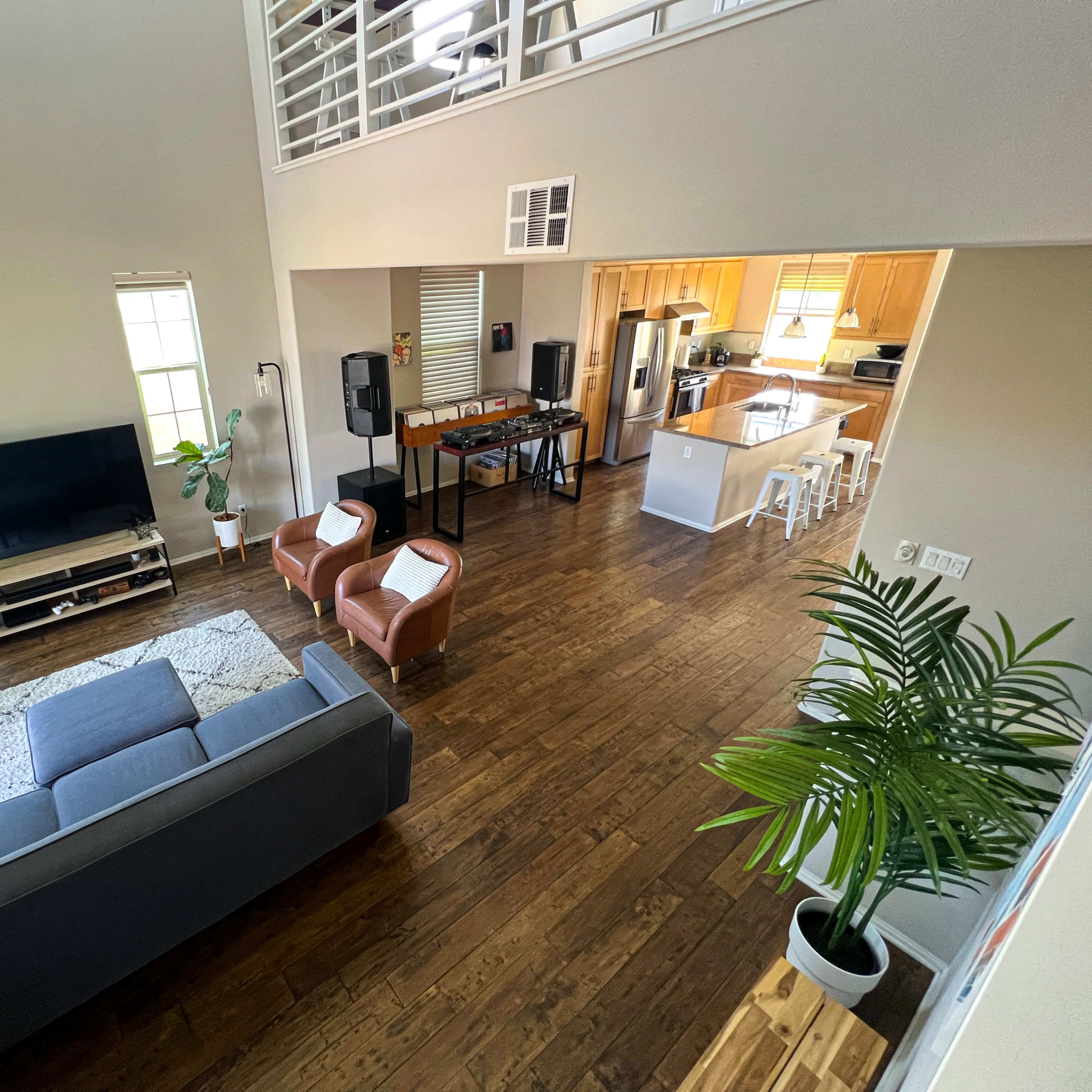 A spacious living room with a grey sofa, two brown chairs, a television, and an open kitchen area in the background.