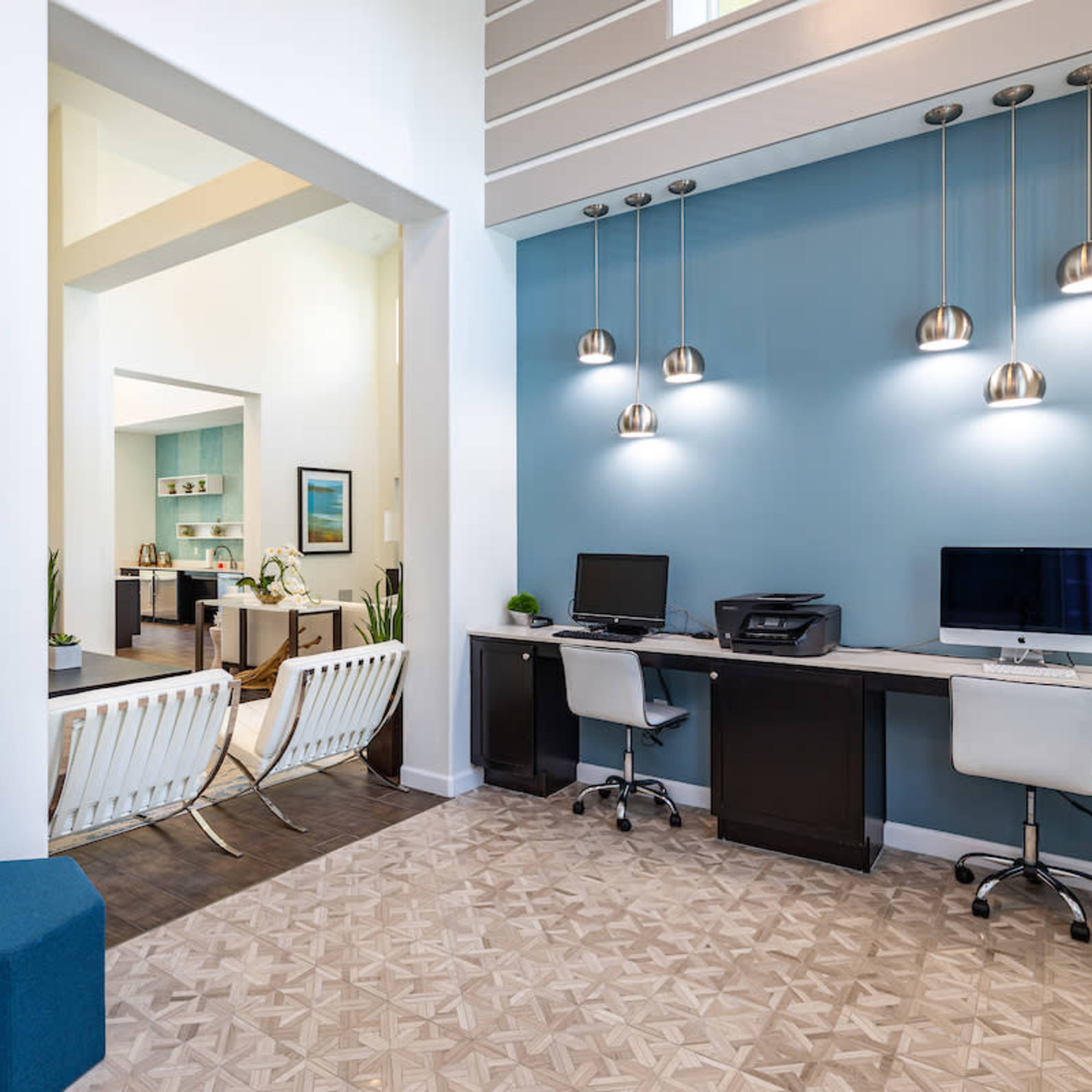 A modern office space with two computers on a black desk and decorative wall pieces, leading to another room with light-colored furnishings.