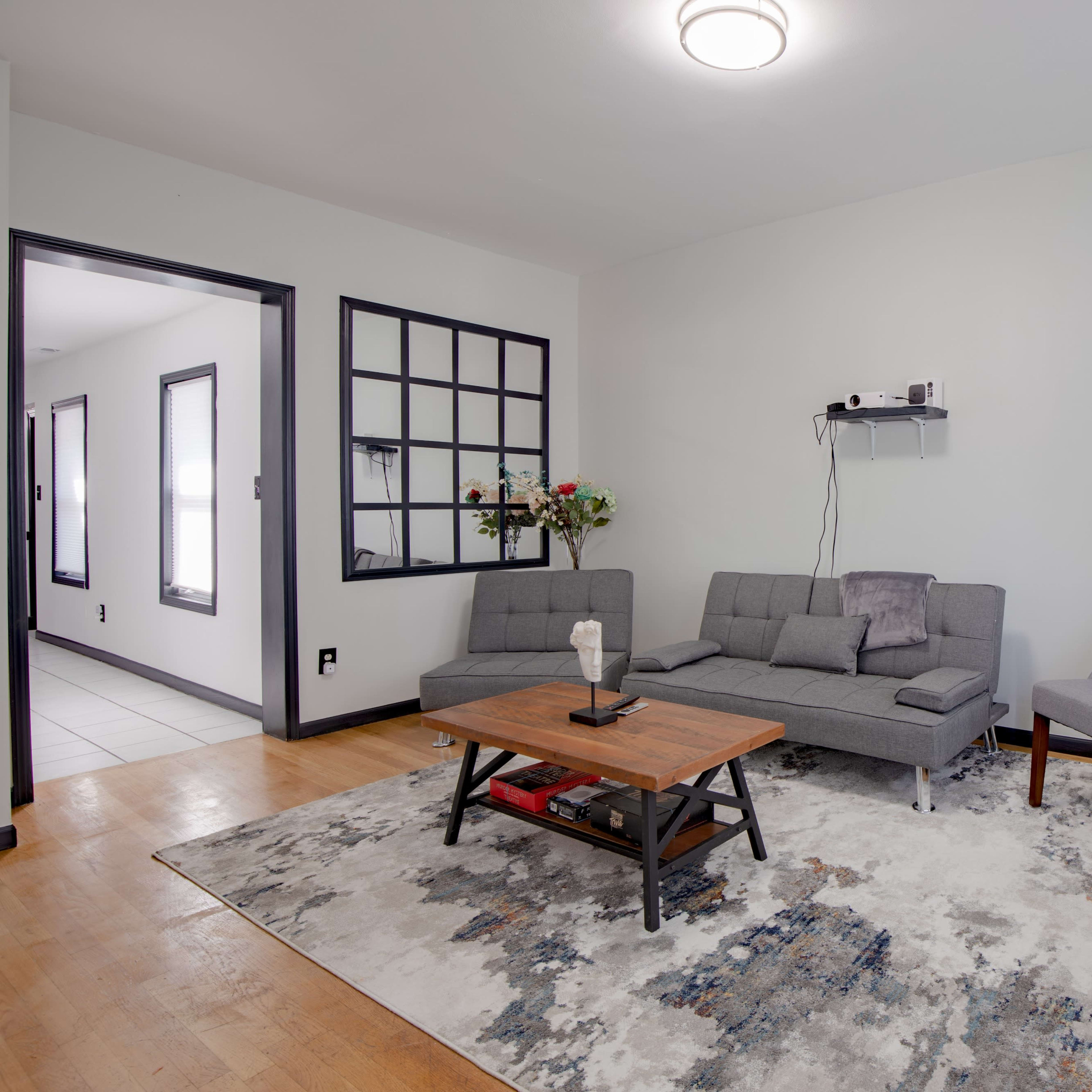 A modern living room features a gray sectional sofa, a wooden coffee table, and a side chair, with a large area rug on the wooden floor and a lamp next to a small table.