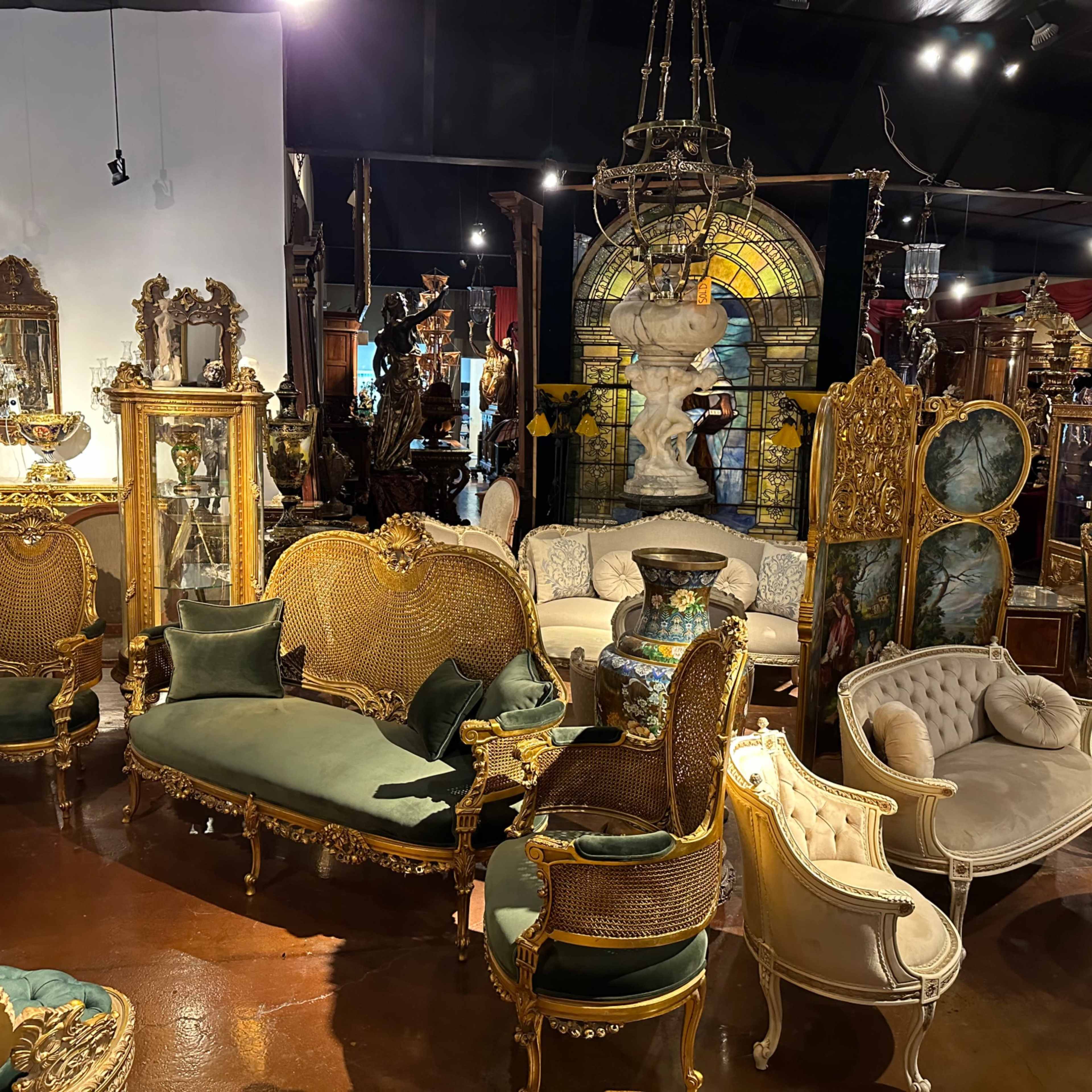 A vintage furniture store filled with ornate chairs, sofas, and decorative mirrors arranged around a stained glass feature.