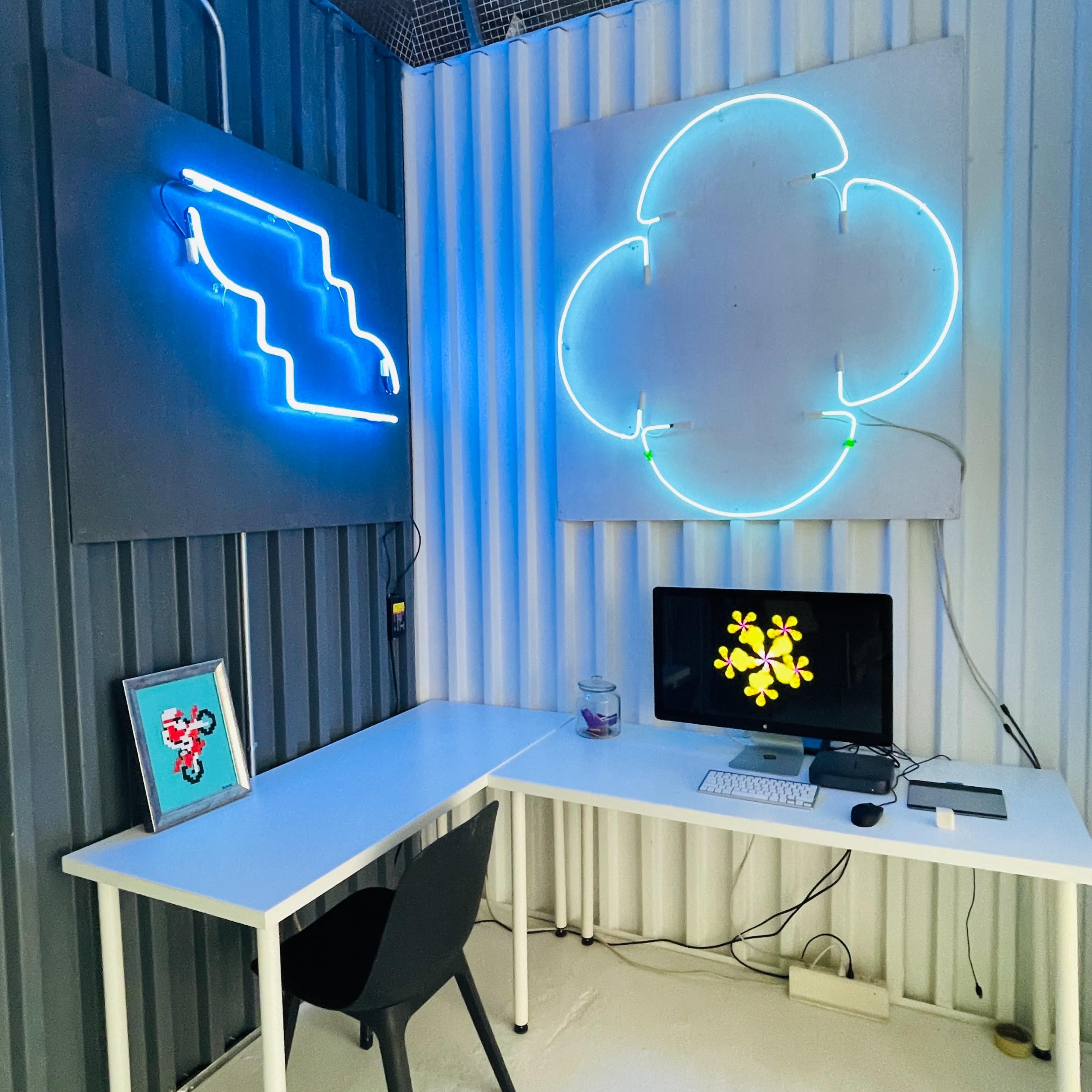 A minimalist workspace with a desk, a computer, and colorful neon light designs on the wall.