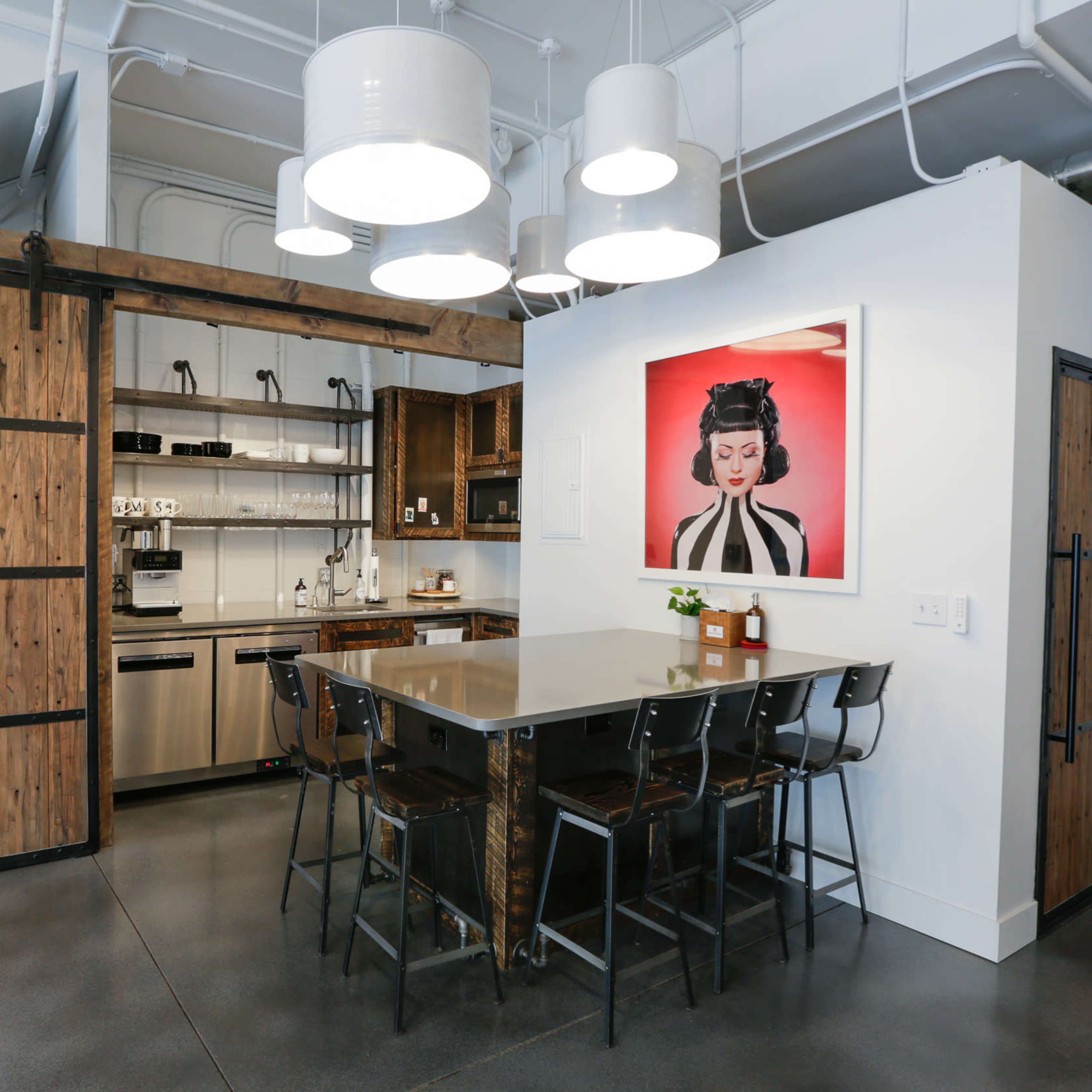 A modern kitchen featuring a wooden sliding barn door, stainless steel appliances, a gray countertop with bar stools, and a framed artwork on the wall.