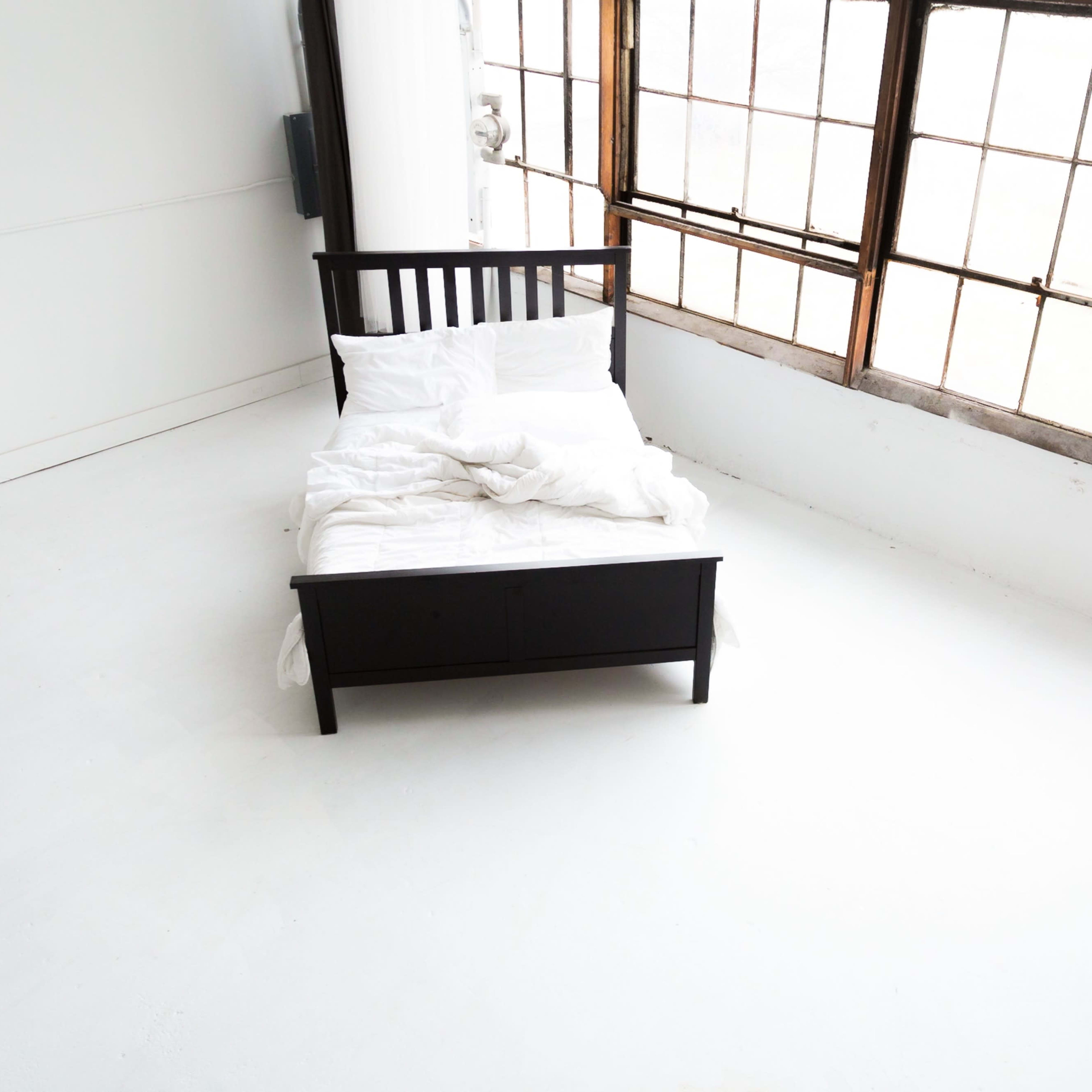 A black bed with white bedding is positioned in a large, sunlit room with tall windows.