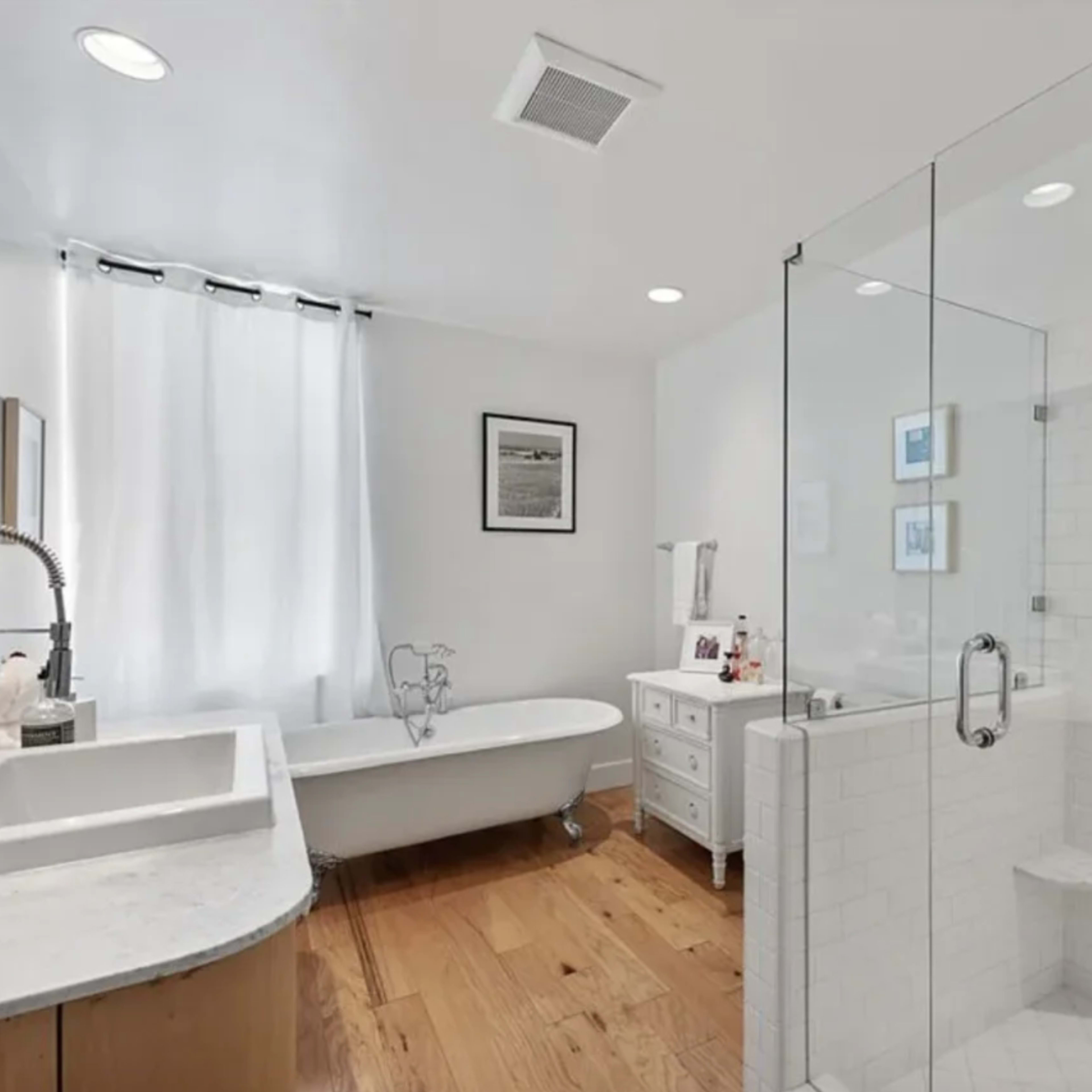 A bright bathroom featuring a freestanding bathtub, a glass shower, and a double sink vanity with a window and natural light.