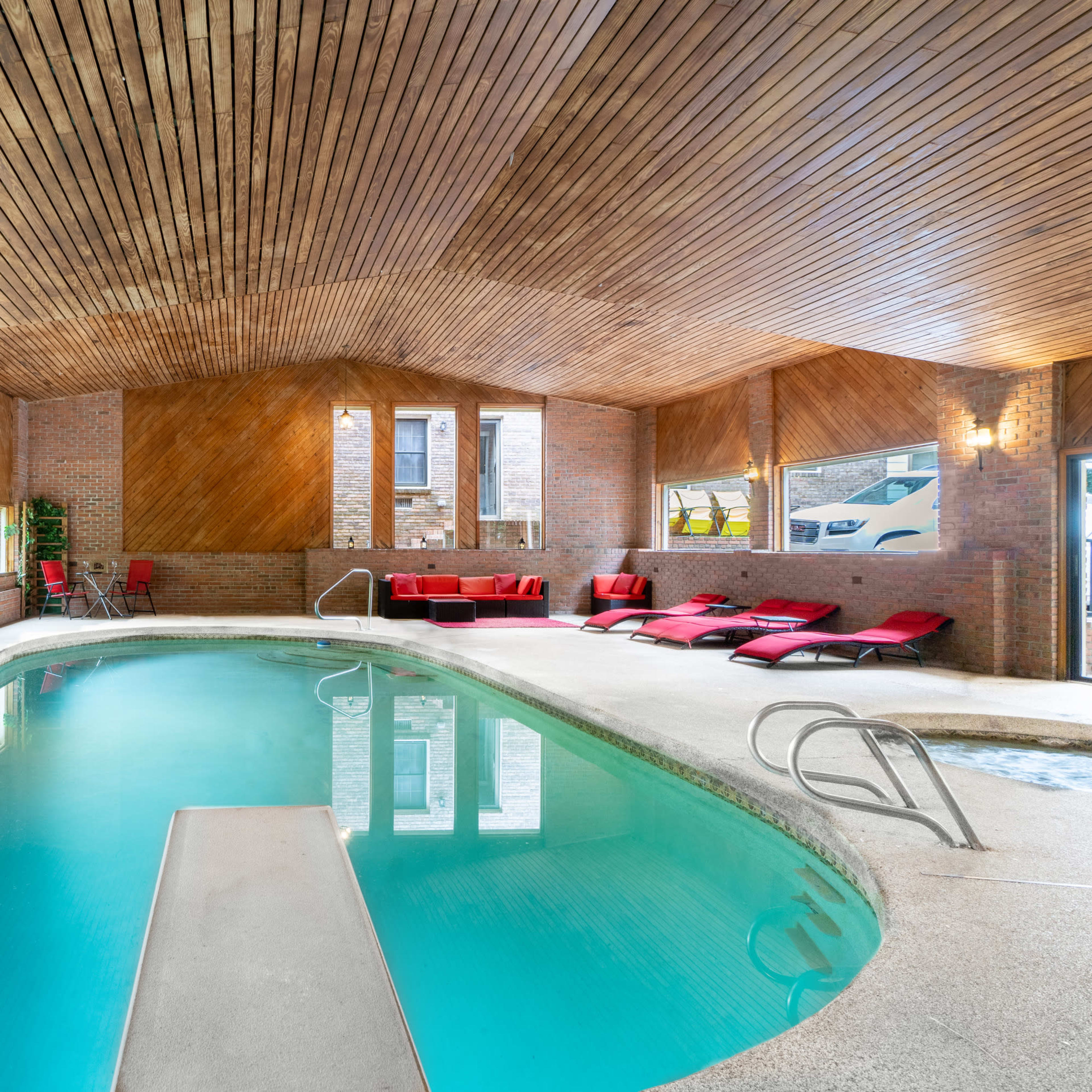 An indoor pool area with a smooth surface and wooden ceiling, featuring red lounge chairs and a welcome sign on the wall.