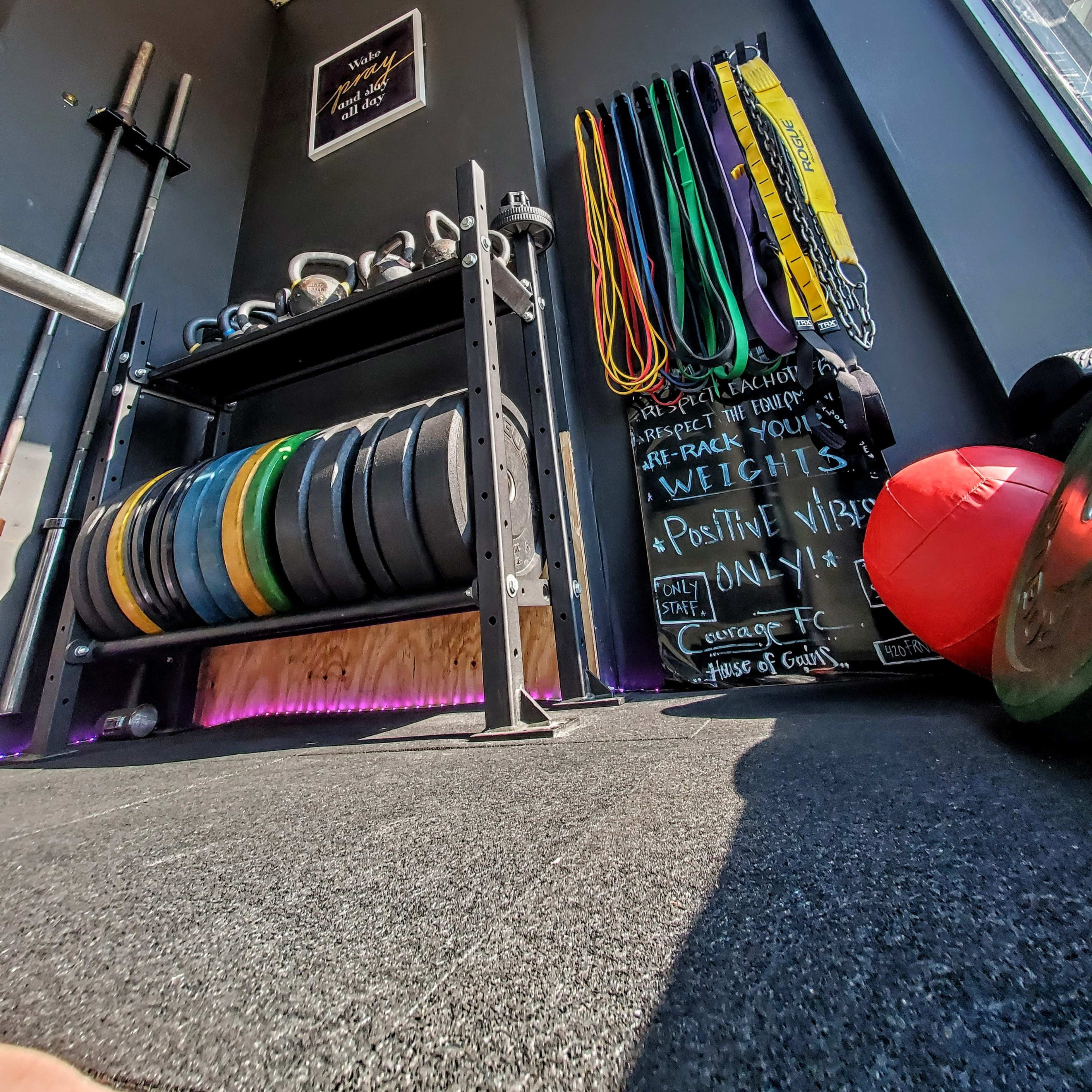 A well-organized gym corner displays weight plates on a rack, resistance bands hanging on the wall, and motivational quotes written on a chalkboard.