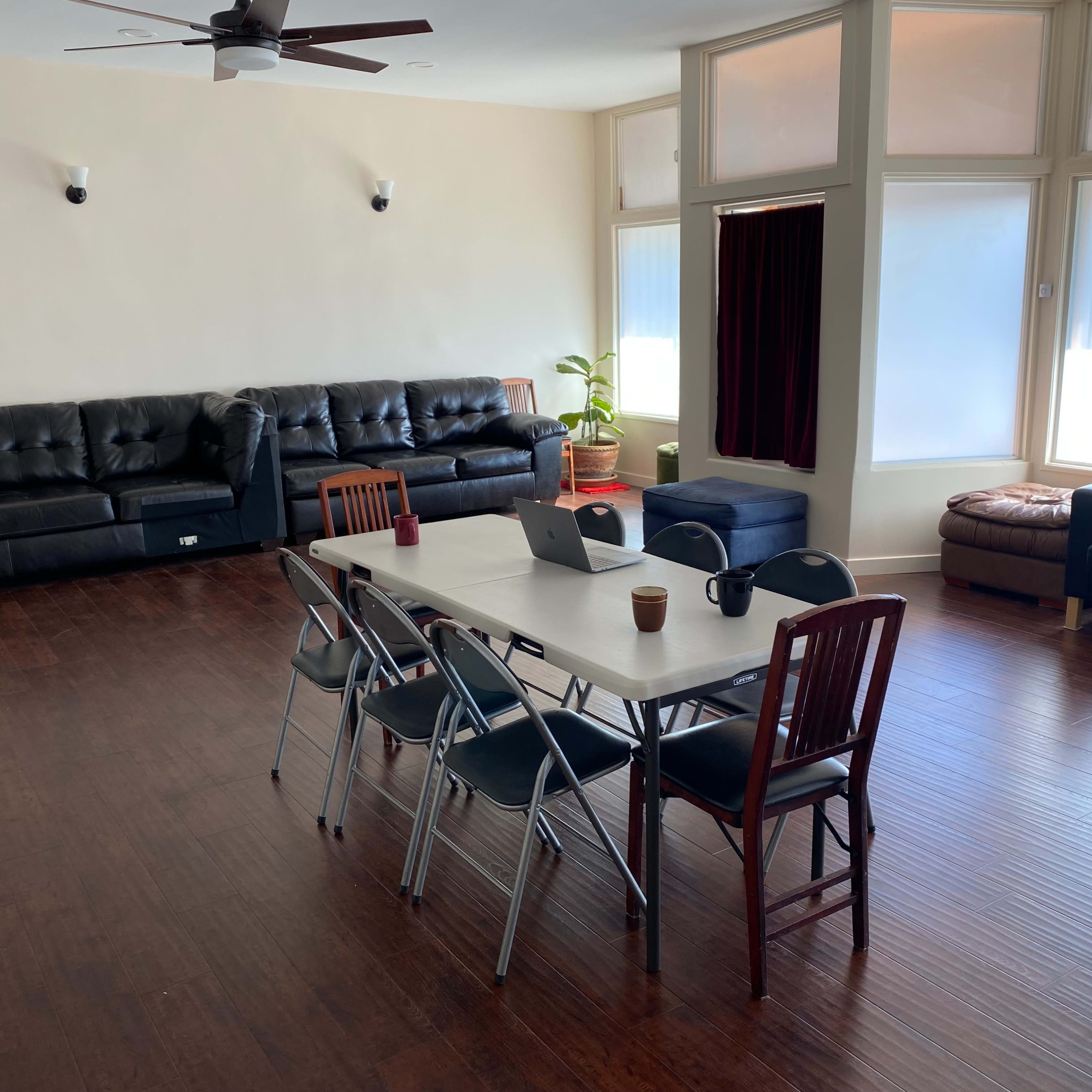 A spacious room furnished with a long table and chairs, a few sofas, and large windows letting in natural light.