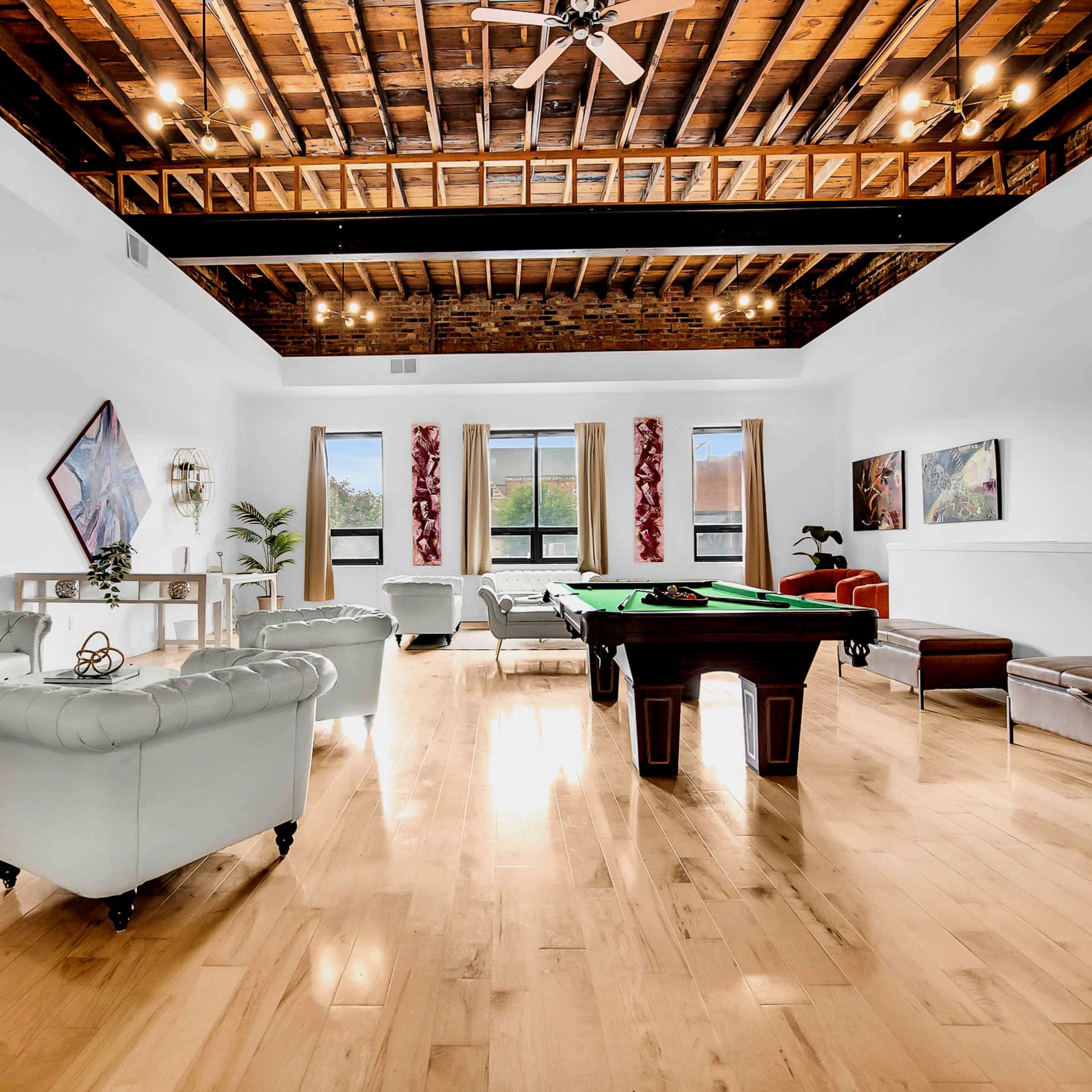 A spacious room with a wooden ceiling, featuring a pool table, leather seating, and colorful wall art.