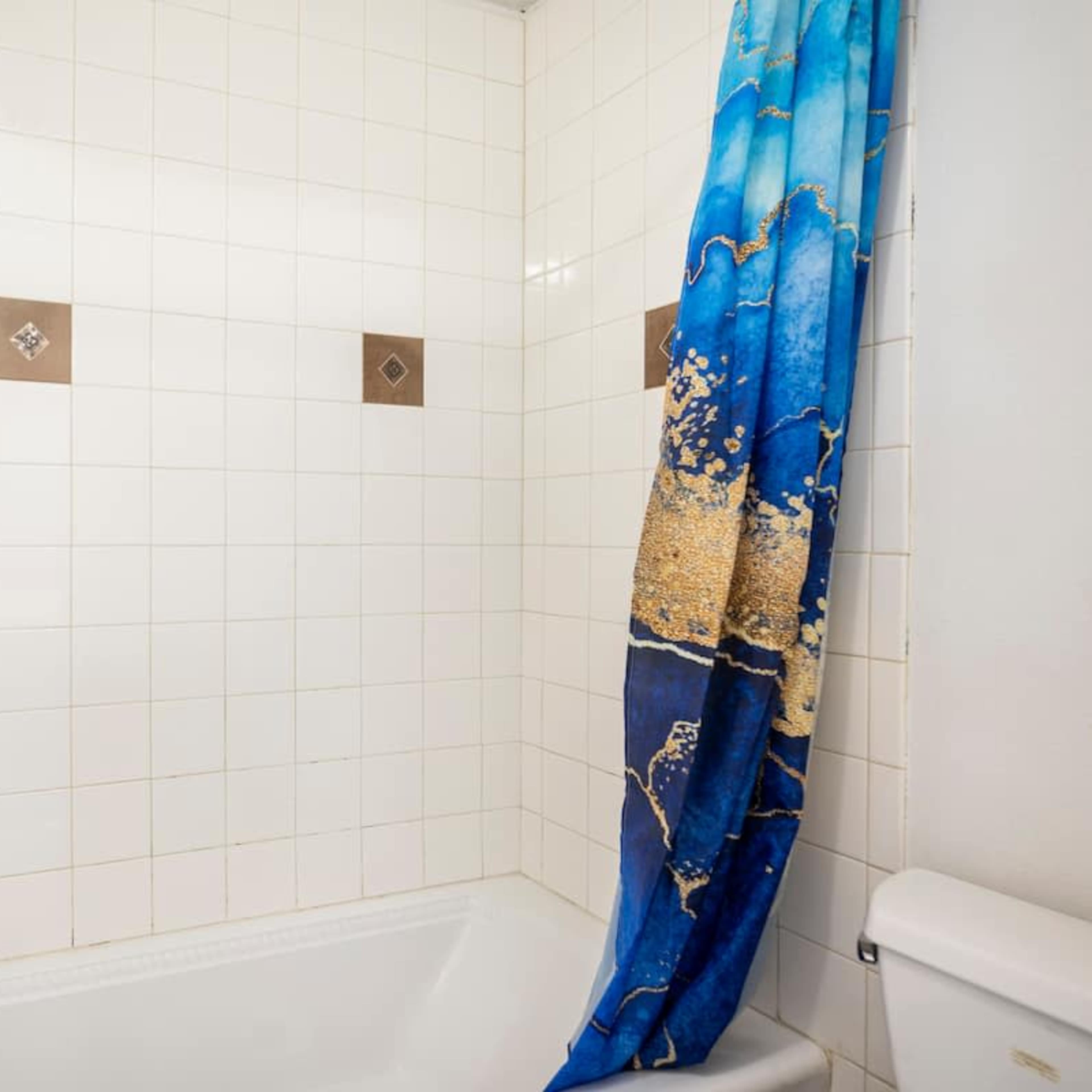 A bathroom with a white tiled shower area, a bathtub, and a blue shower curtain decorated with an oceanic design.