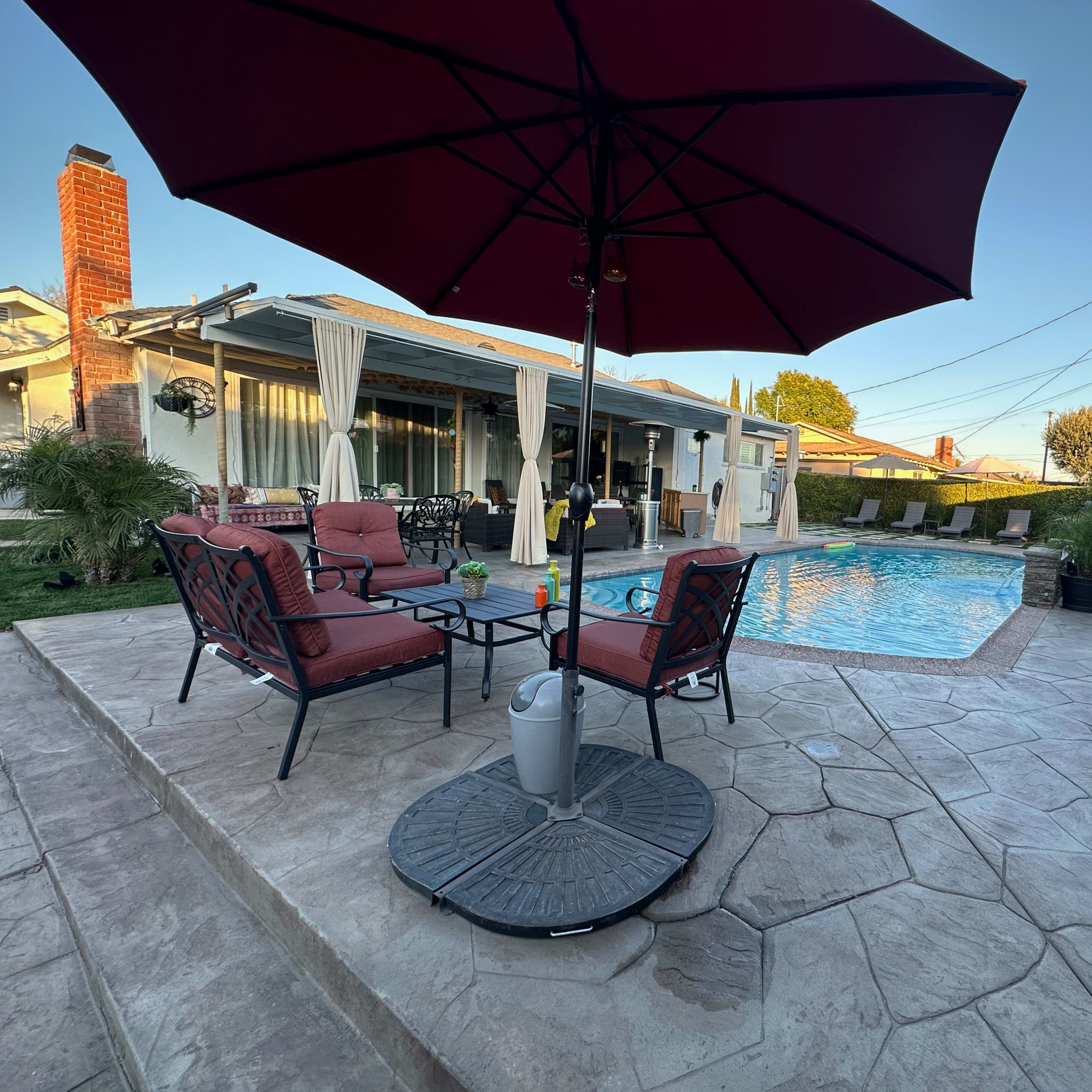 A swimming pool surrounded by patio seating and an umbrella, with a house and power lines in the background.