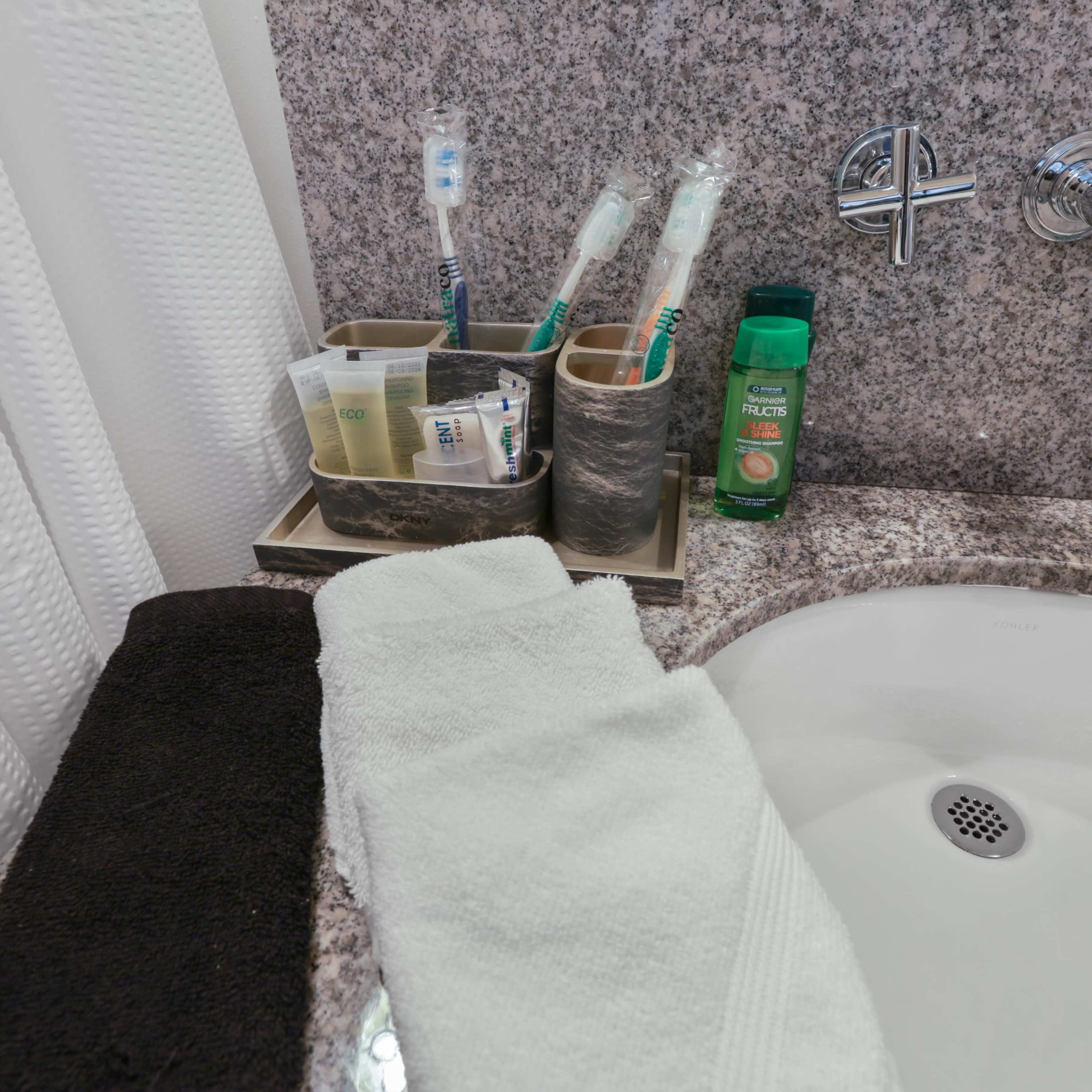 A bathroom countertop with a sink, toothbrushes in holders, toiletries, and two towels.