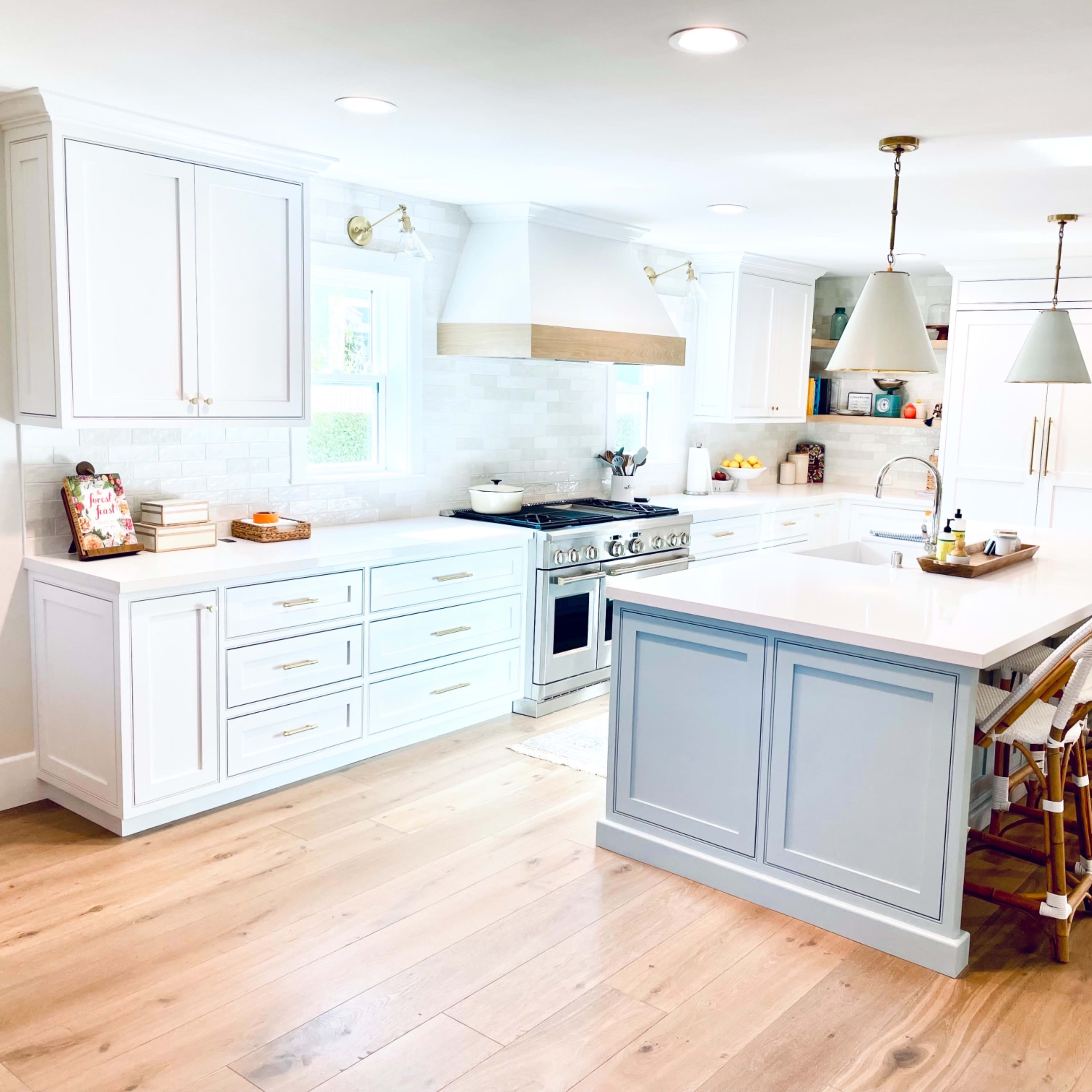 A bright, modern kitchen features white cabinetry, a large island with seating, and stainless steel appliances.