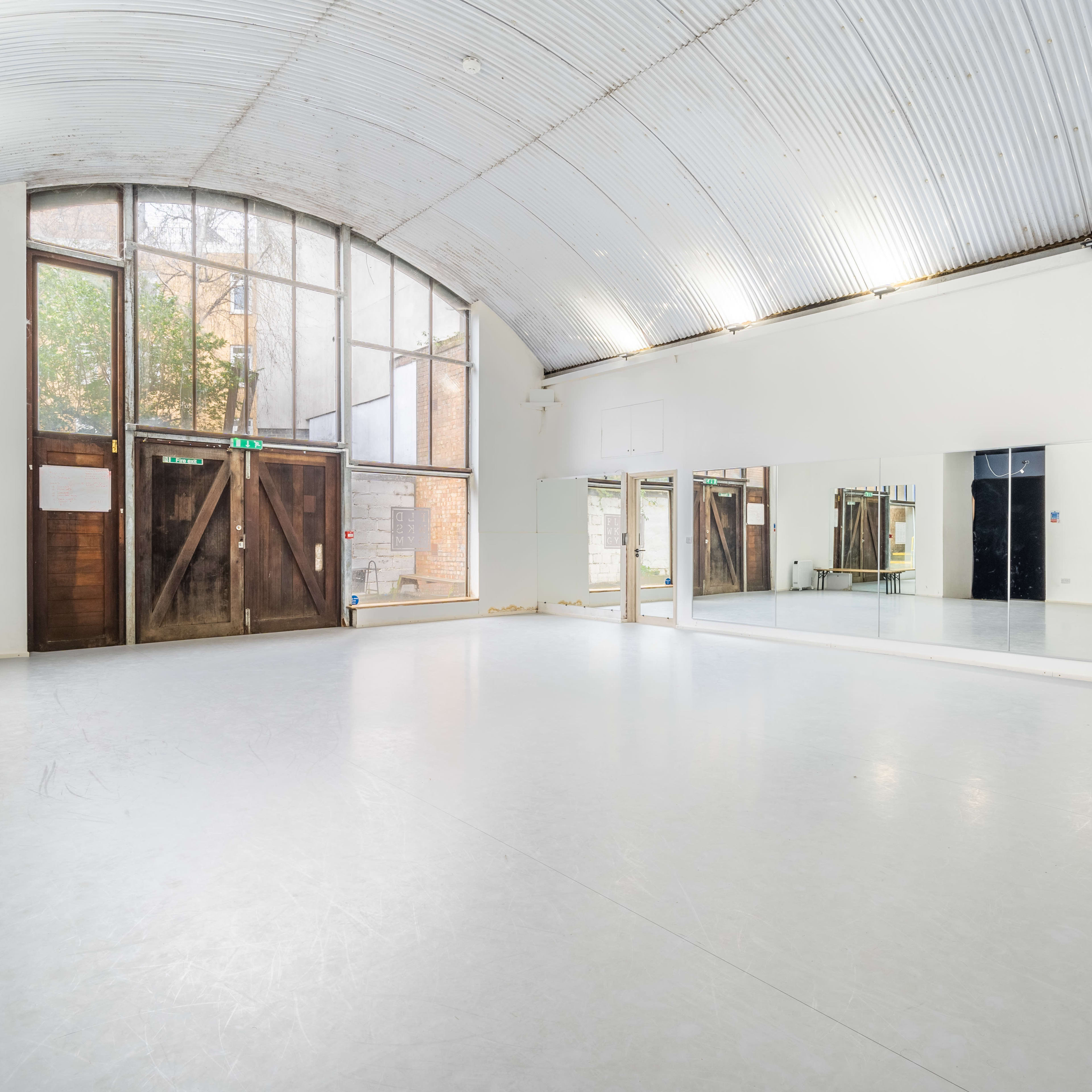 An empty dance studio with a high arched ceiling, large windows, and a mirrored wall.