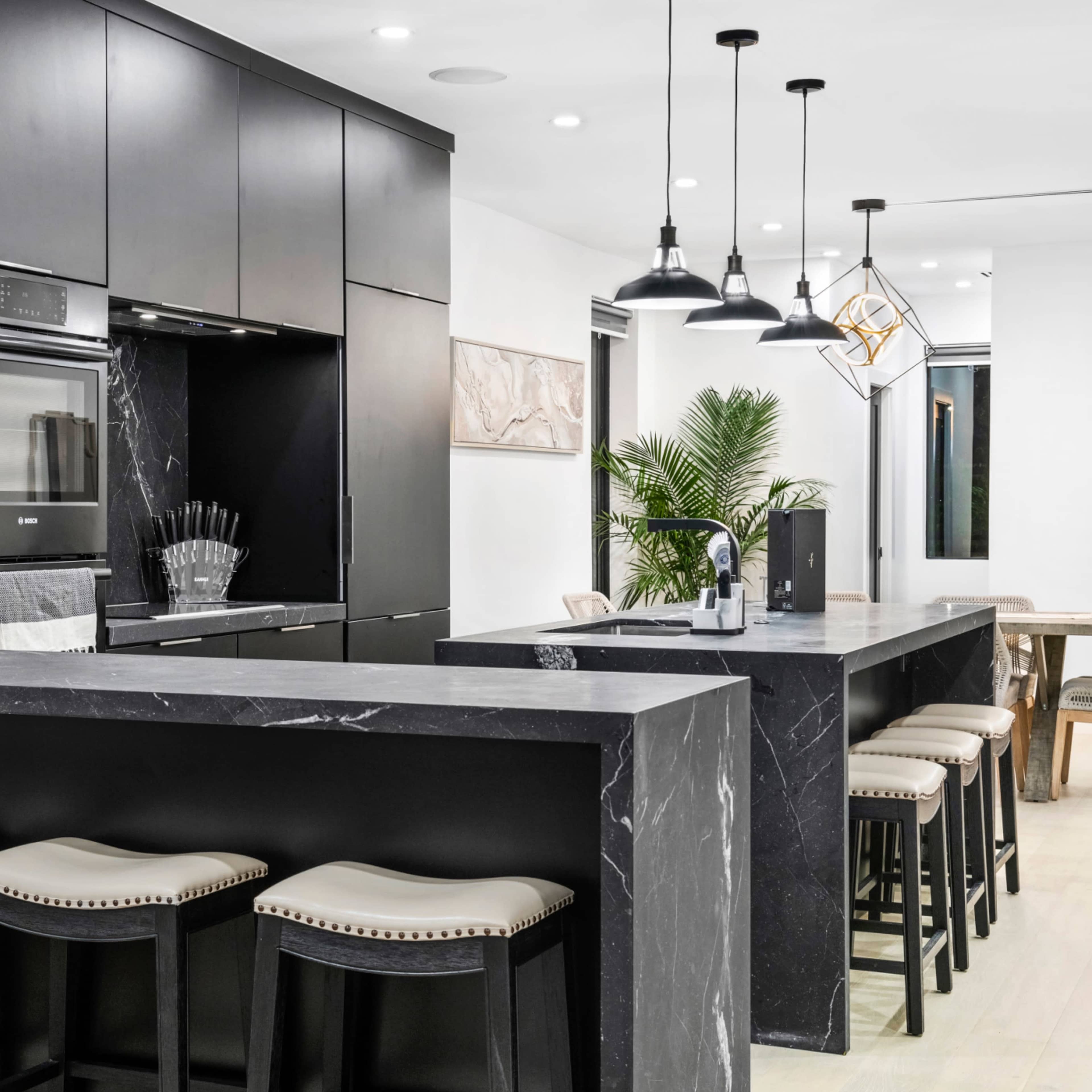 A modern kitchen featuring black cabinetry, marble countertops, and bar seating with beige stools.
