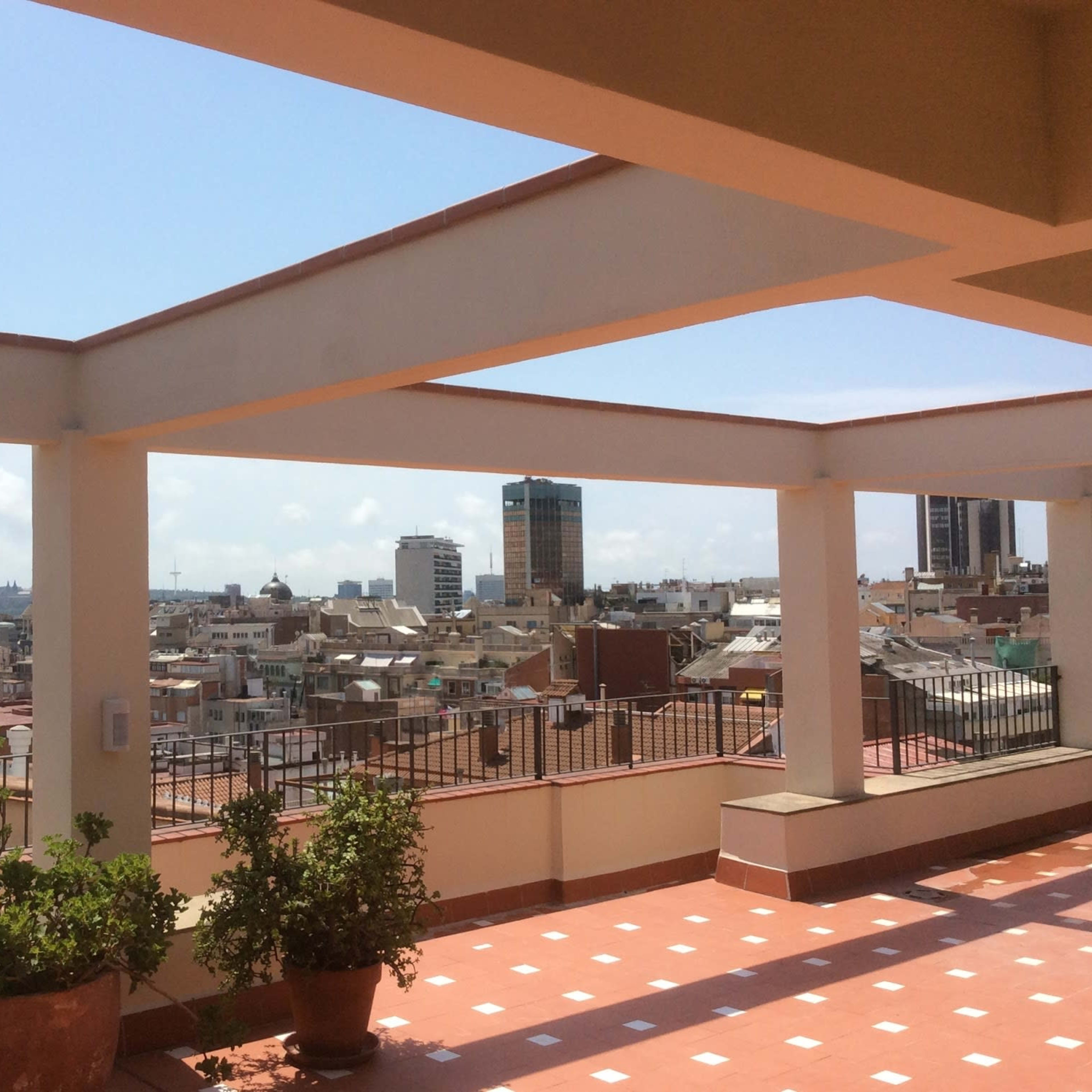 A rooftop terrace with a view of a city skyline featuring several high-rise buildings and a clear sky.