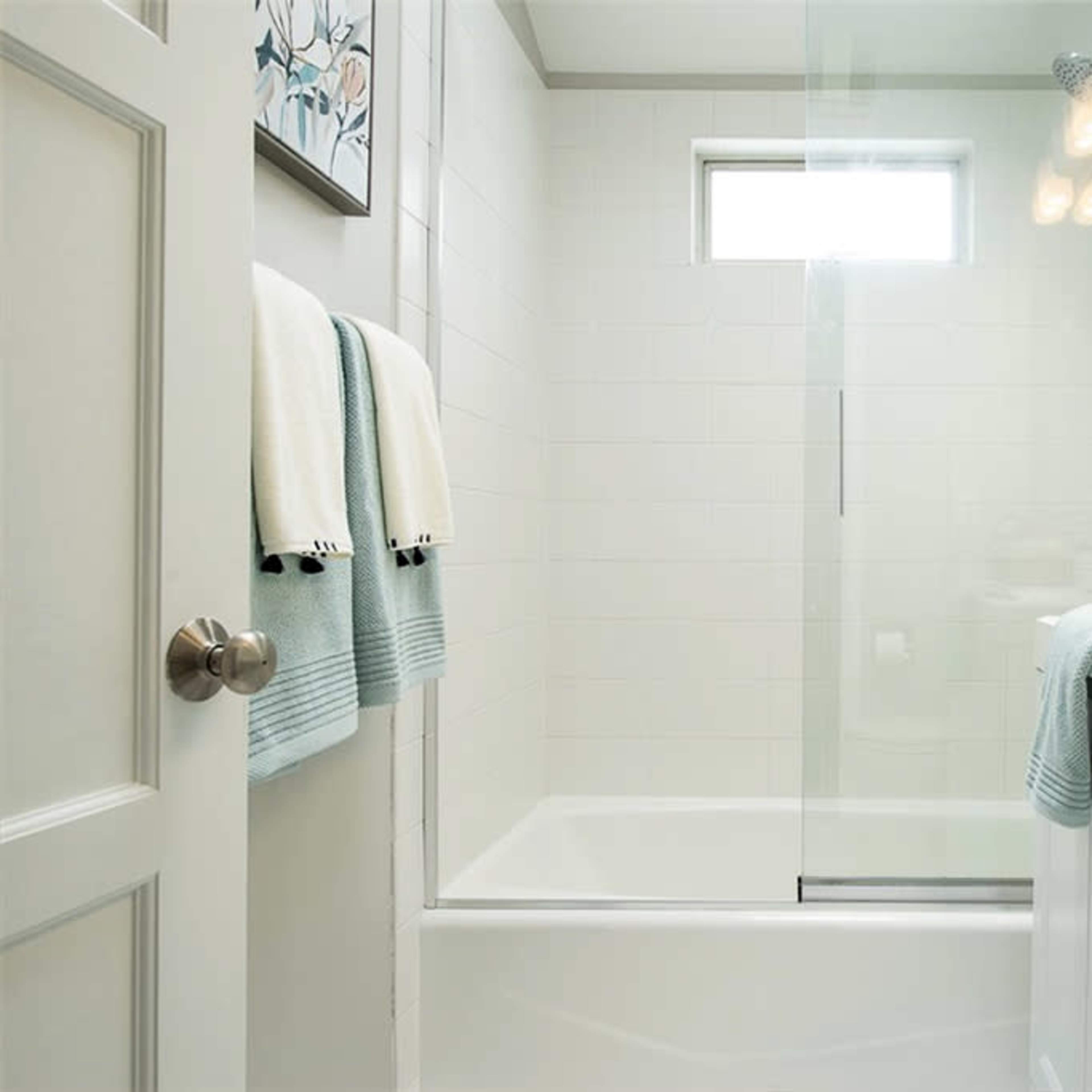 A modern bathroom with a glass shower, a white bathtub, a vanity with a sink, and light-colored towels hanging on a rack.