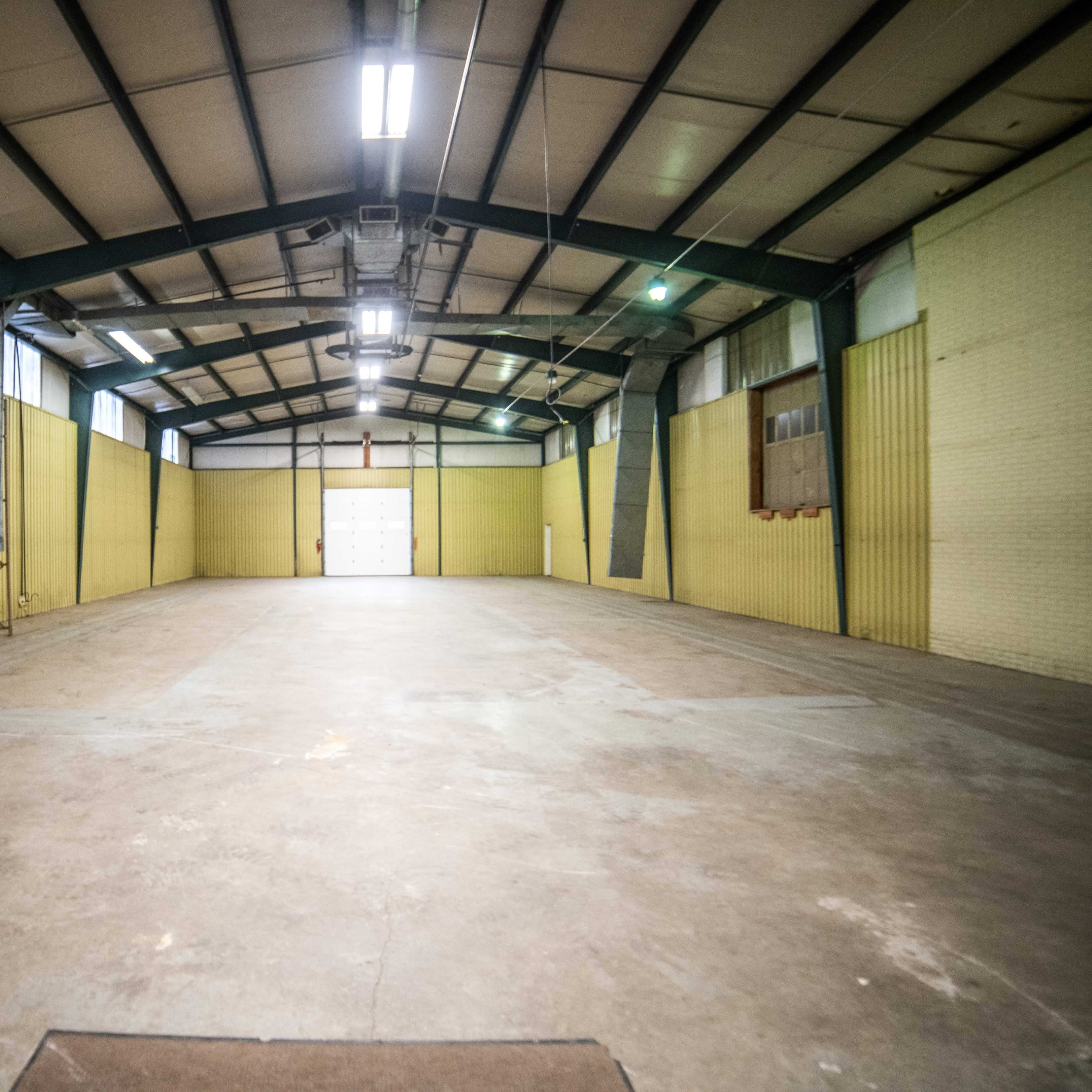 An empty industrial space with yellow walls and a high ceiling, featuring a large, open concrete floor and a rear door.