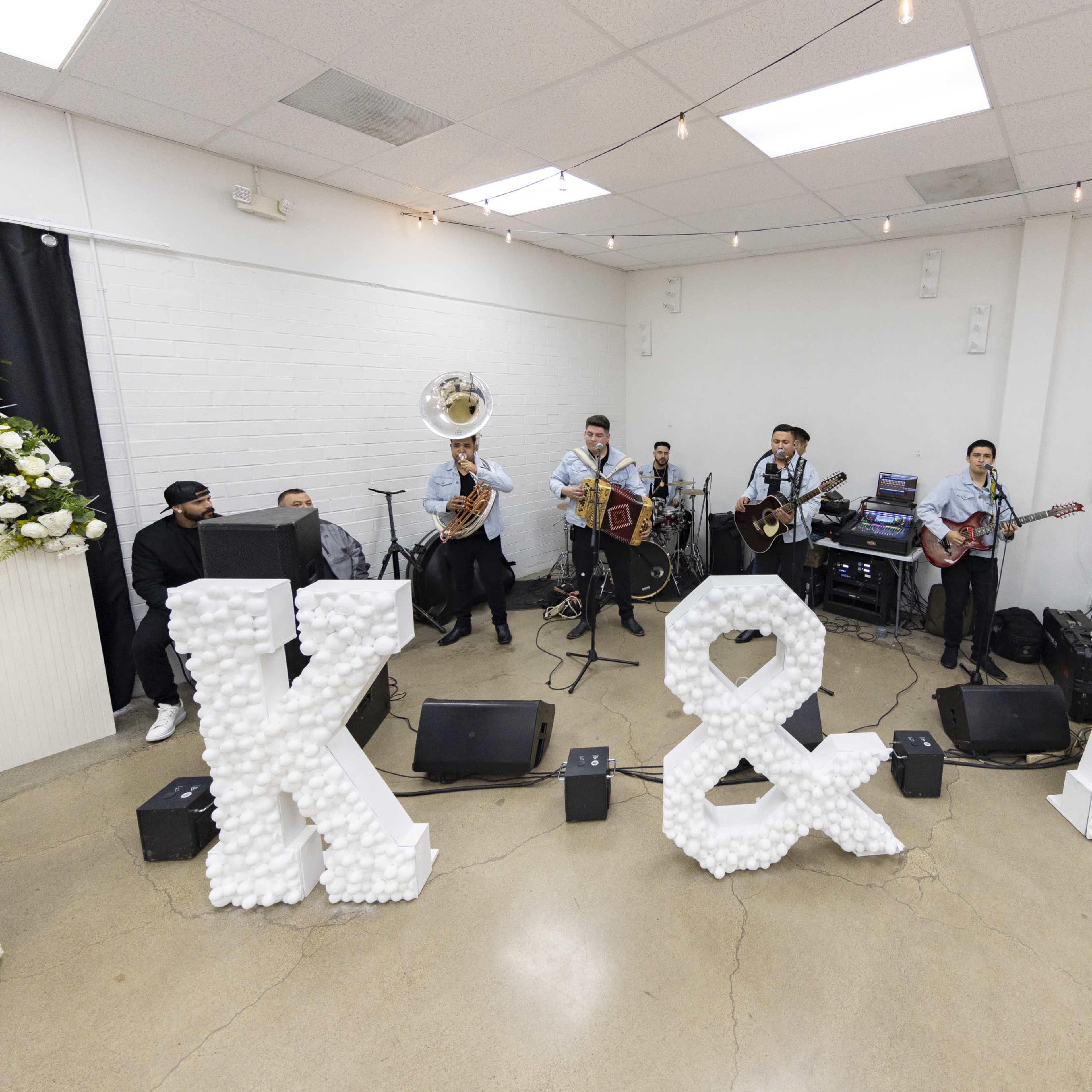 A band performs on a small stage in front of large decorative letters spelling "K & A," surrounded by musical instruments and sound equipment.