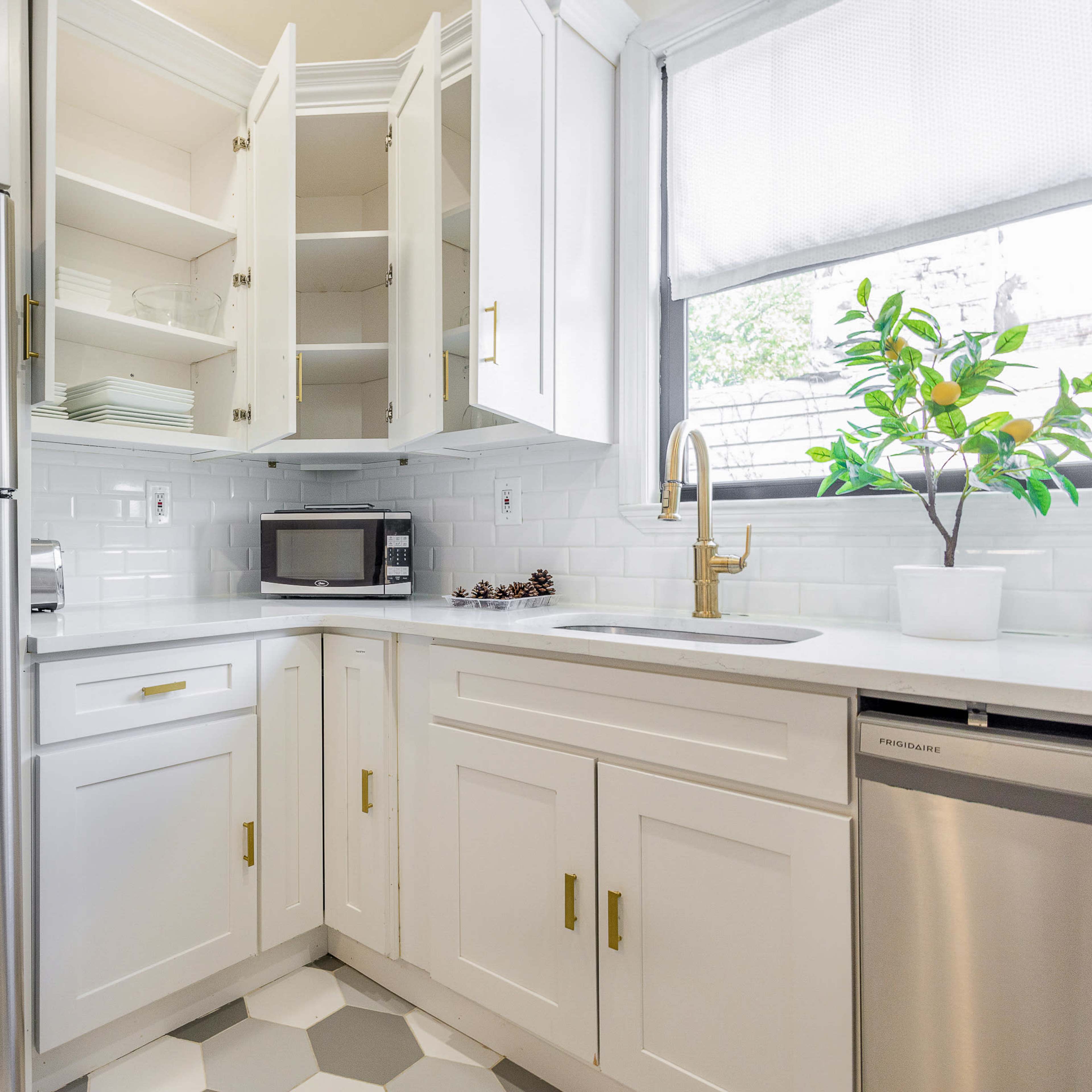 A modern kitchen with white cabinets, a stainless steel refrigerator, a microwave, and a sink in a corner layout featuring hexagonal floor tiles.