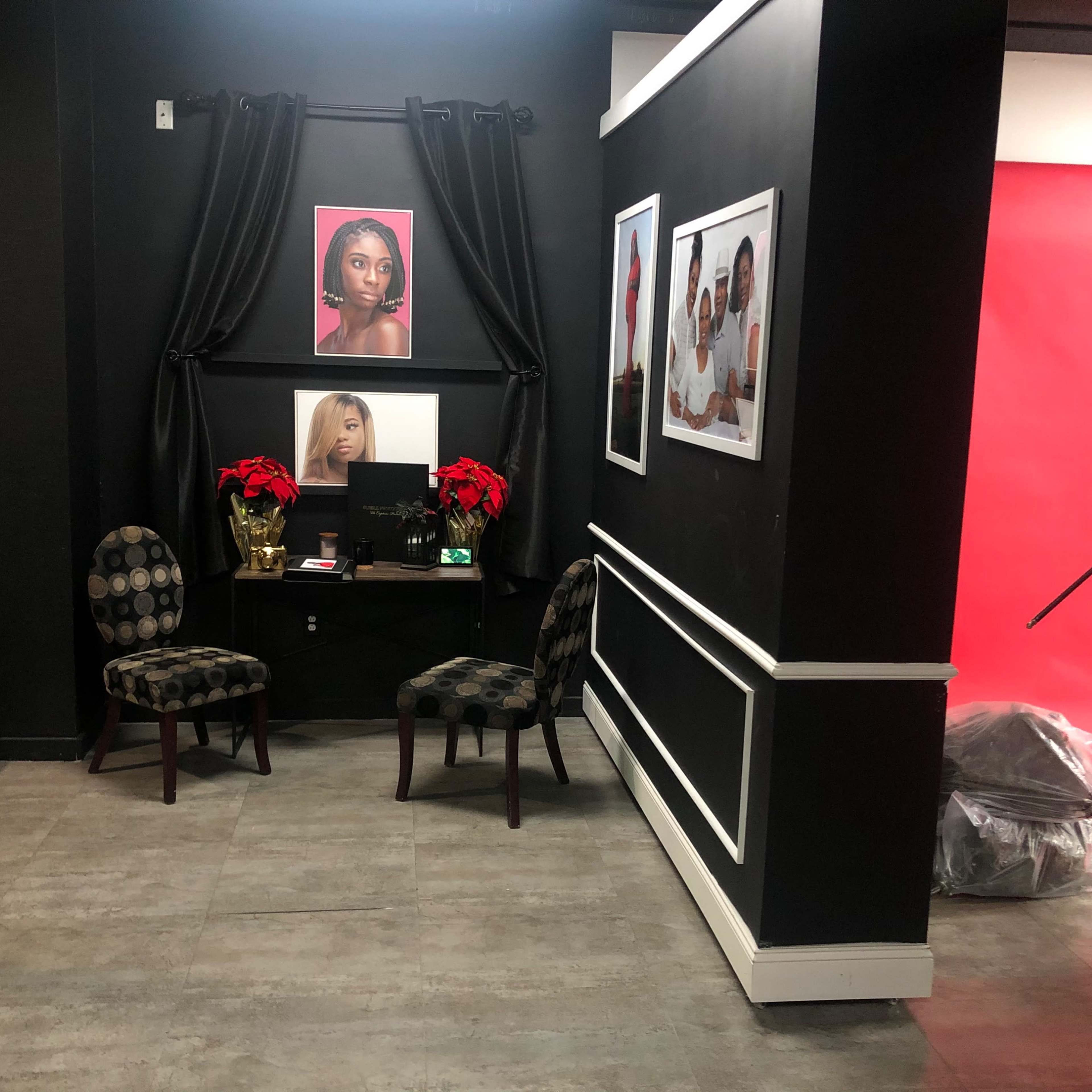 A small studio corner with two patterned chairs, a table adorned with holiday decorations, and framed portraits on the wall, backed by a red backdrop.