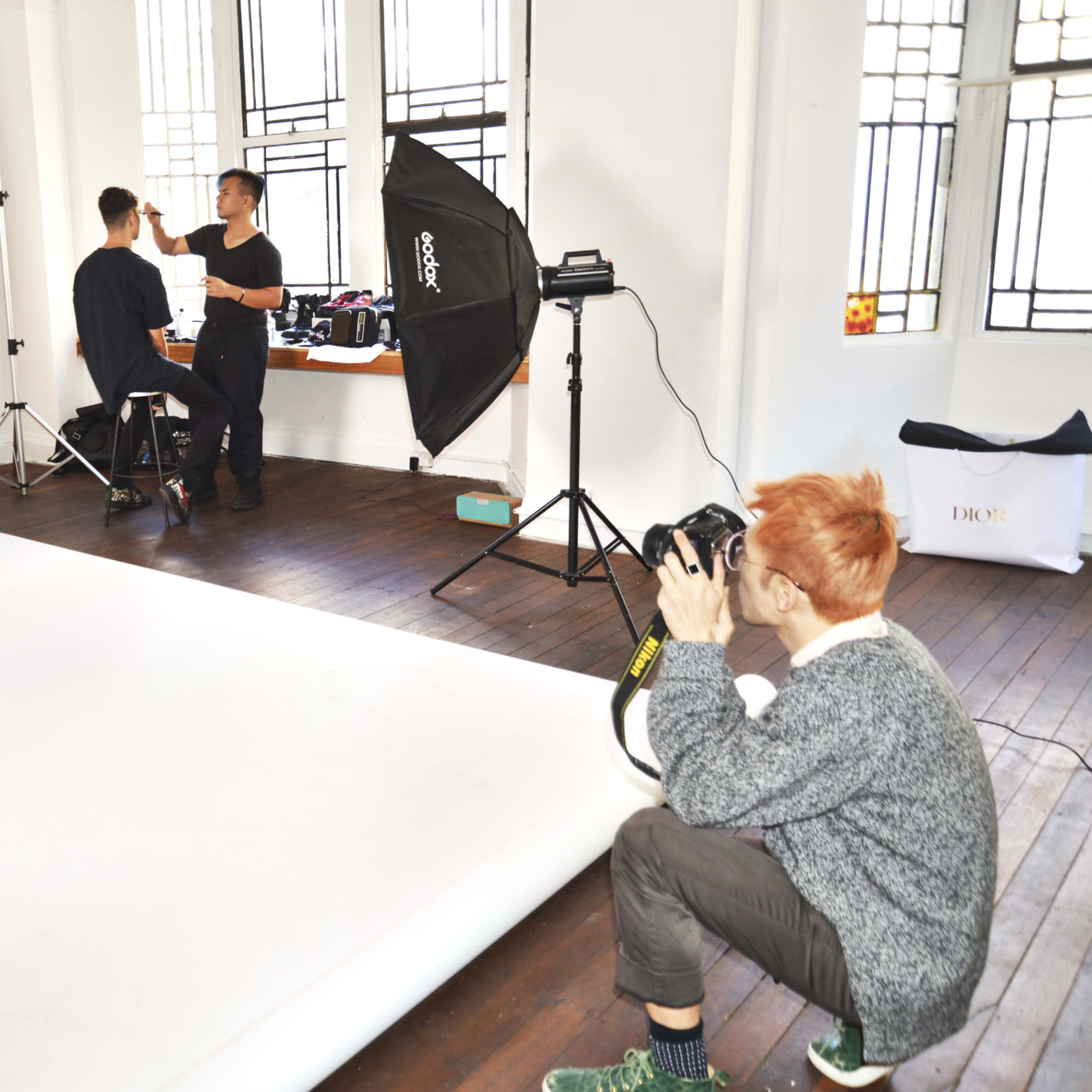 A photographer captures a model posing in a studio while another person adjusts equipment.
