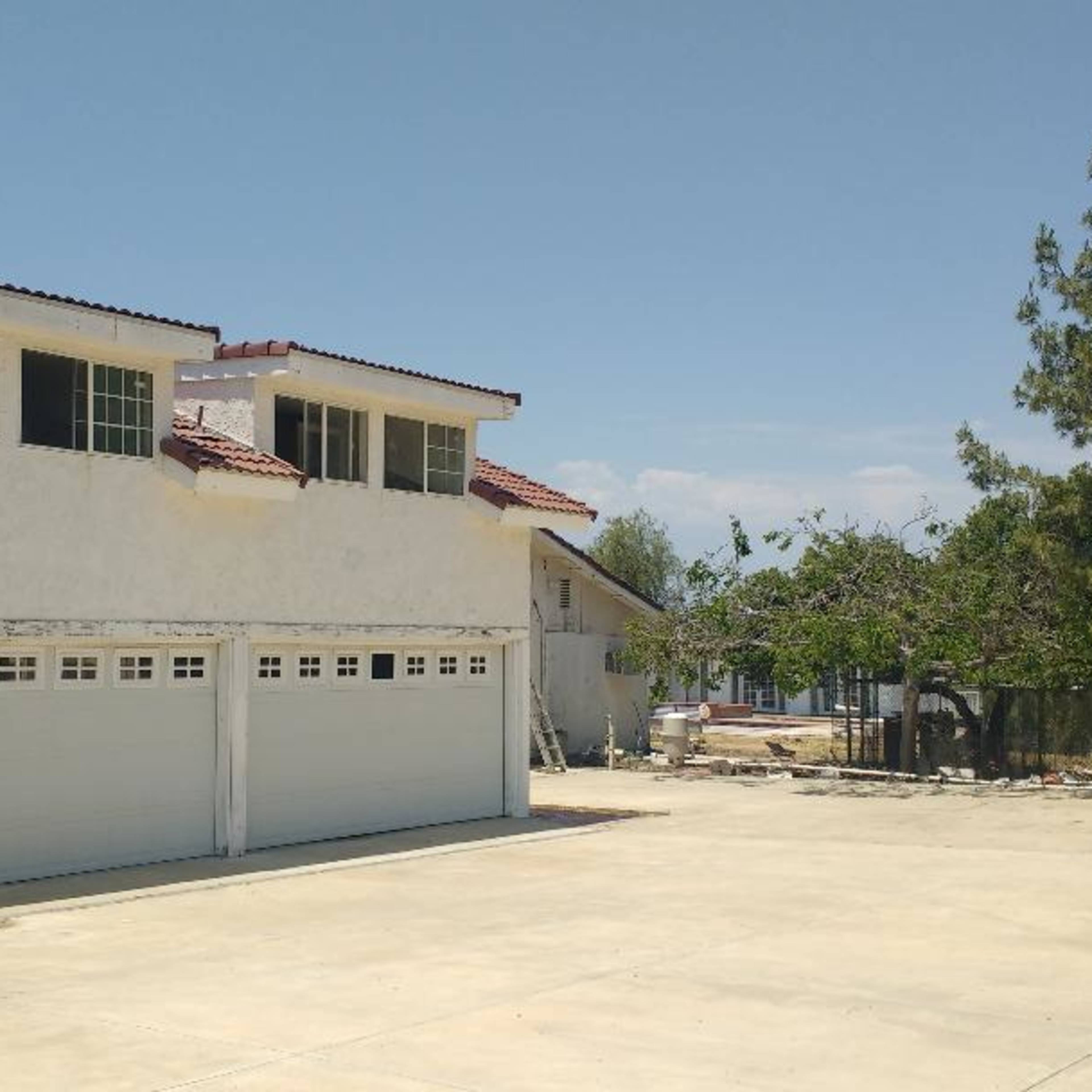 A two-story house with a white exterior and a red-tiled roof features a double garage and a concrete driveway.