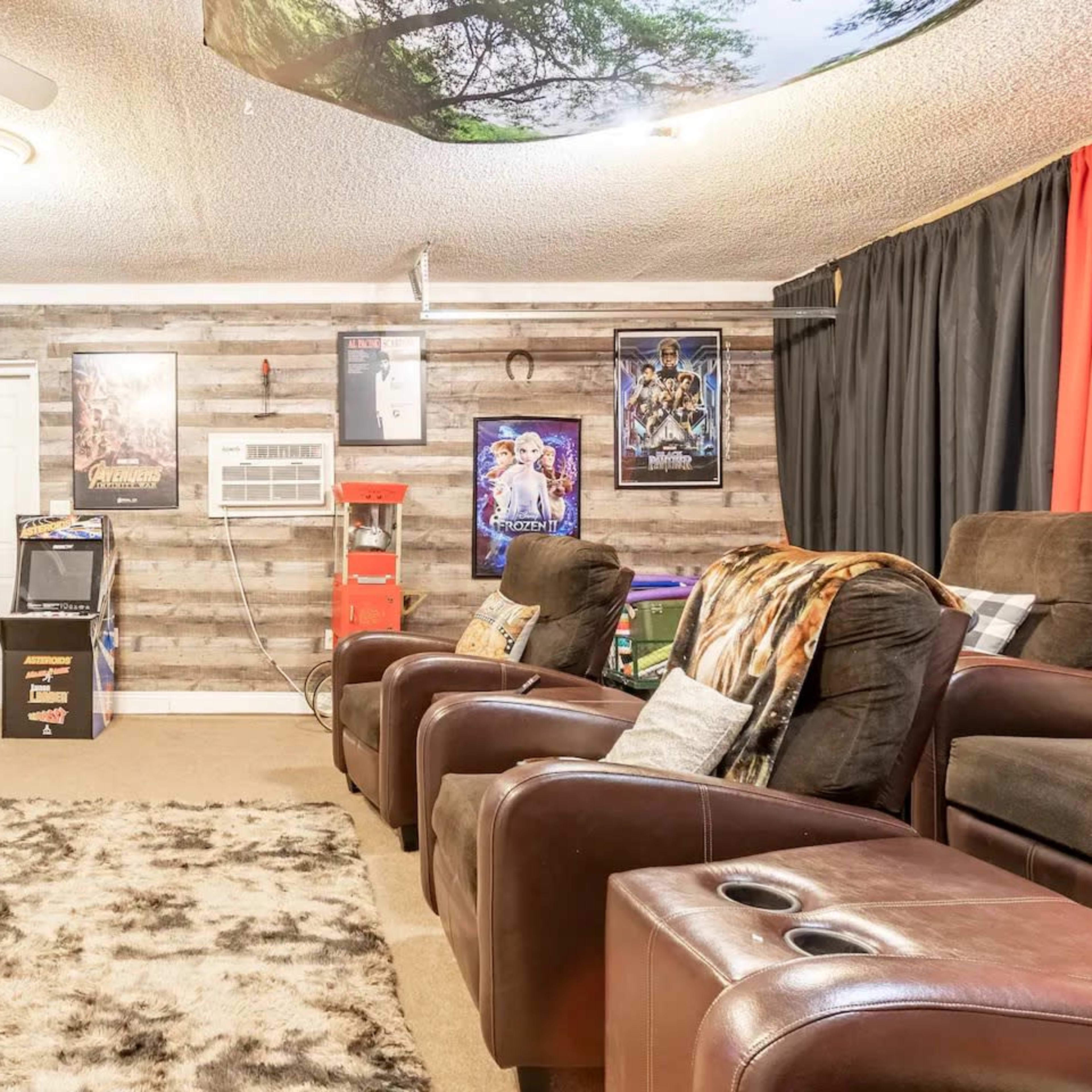 The room features a home theater setup with plush brown recliners, a large screen on the wall, and decorative movie posters.