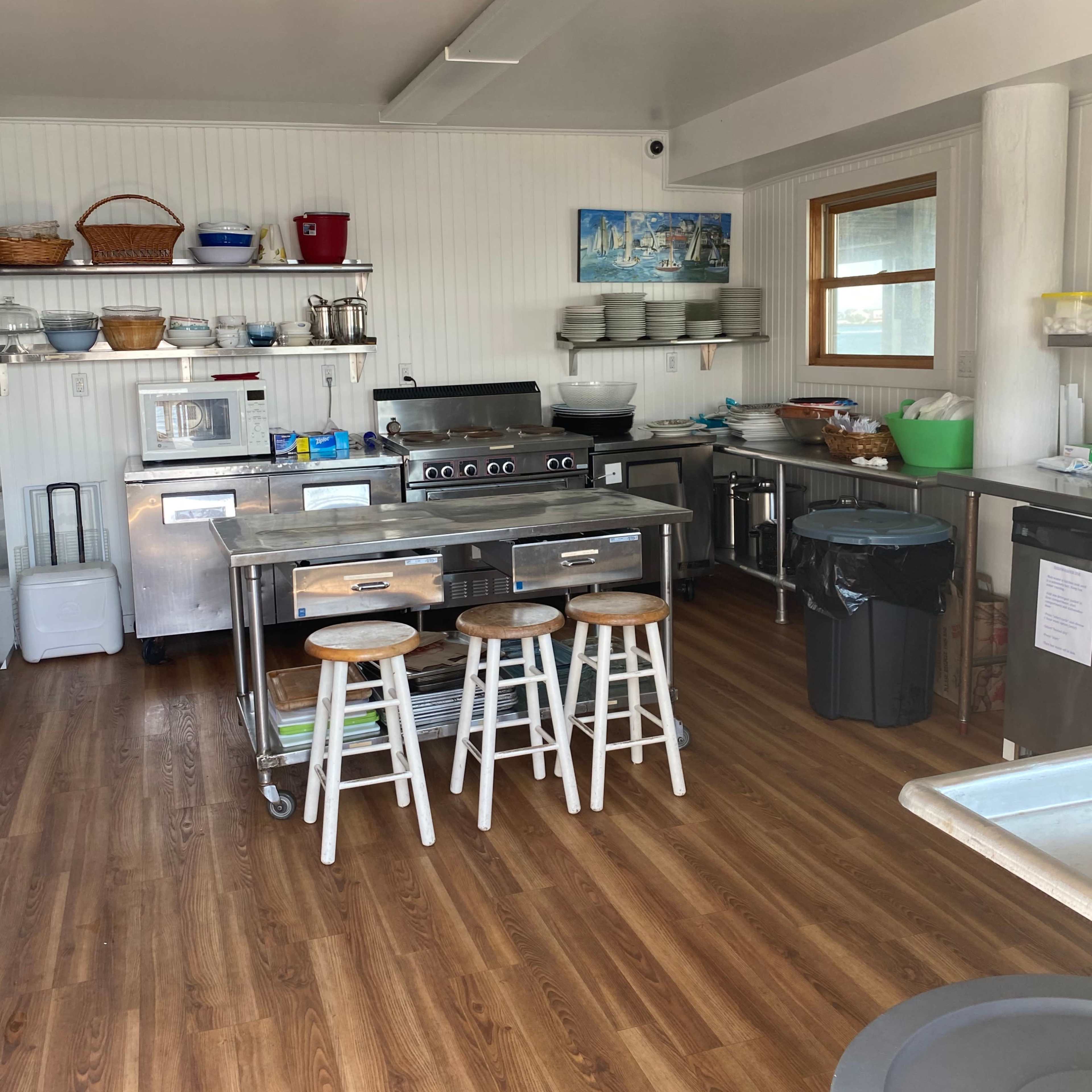A clean, organized kitchen with stainless steel appliances, wooden flooring, and several shelves stocked with kitchenware.