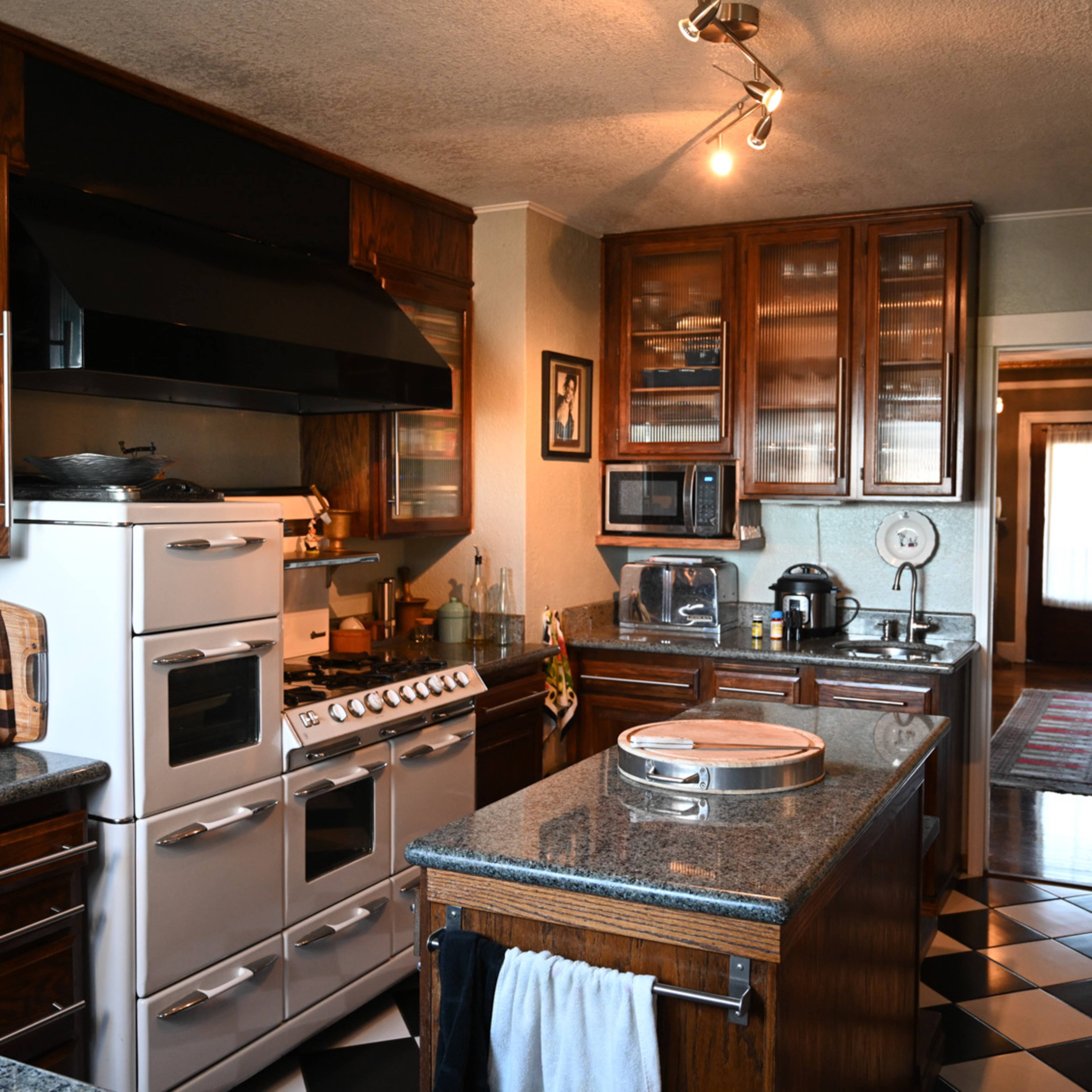 The kitchen features dark wood cabinets, a stainless steel refrigerator, and a mix of black and white checkerboard flooring.