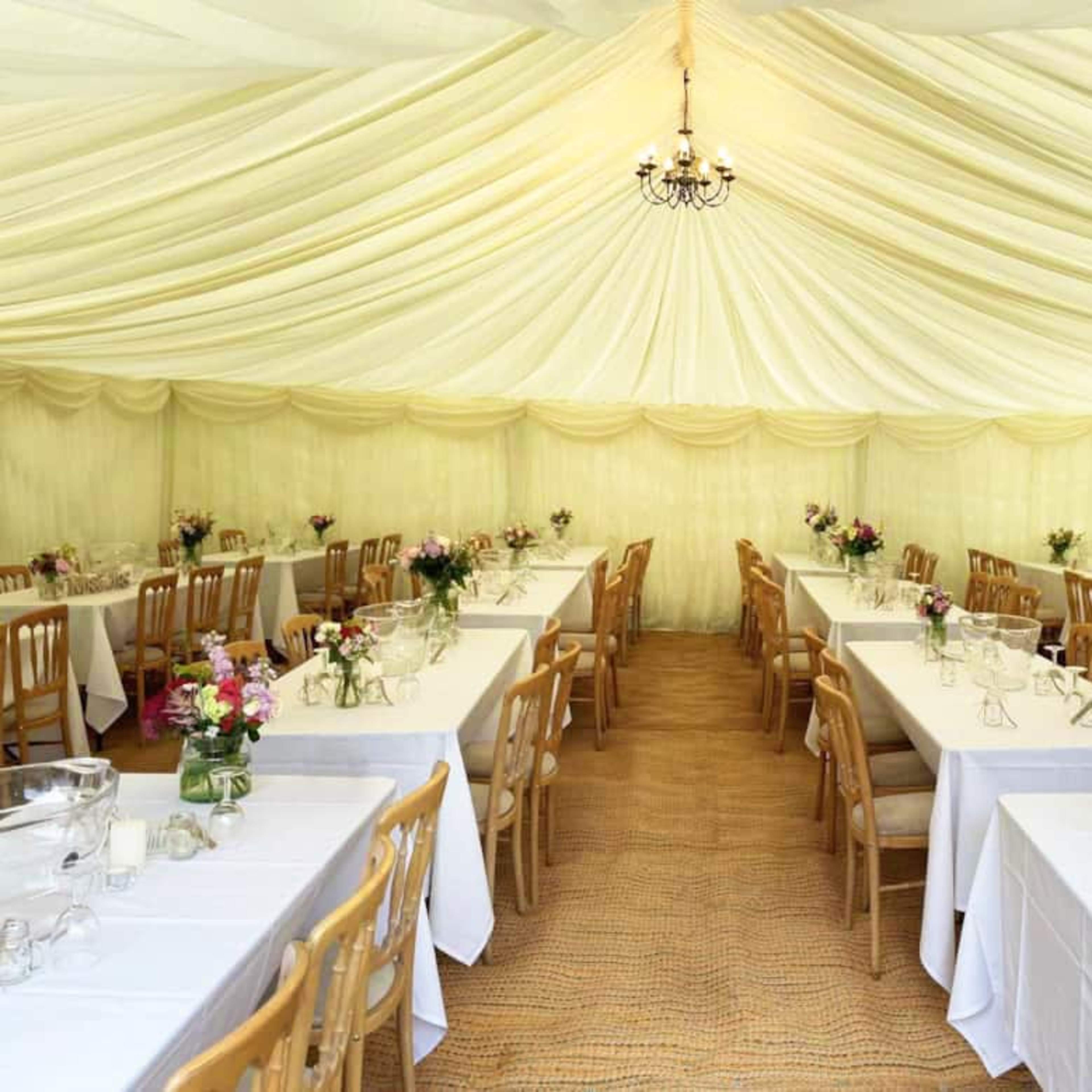 A large, elegantly arranged tent features several long tables with white tablecloths and floral centerpieces.