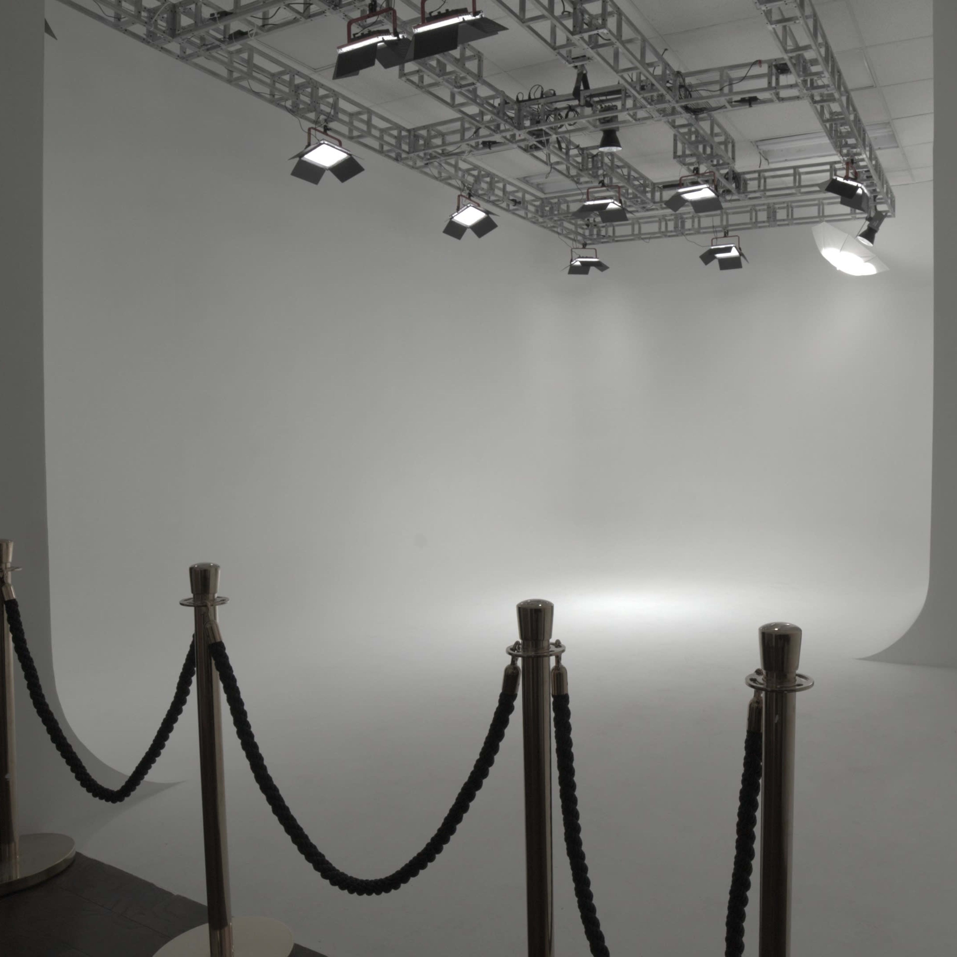 A spacious, empty studio with a seamless white backdrop, lighting rigs, and a velvet rope barrier at the entrance.