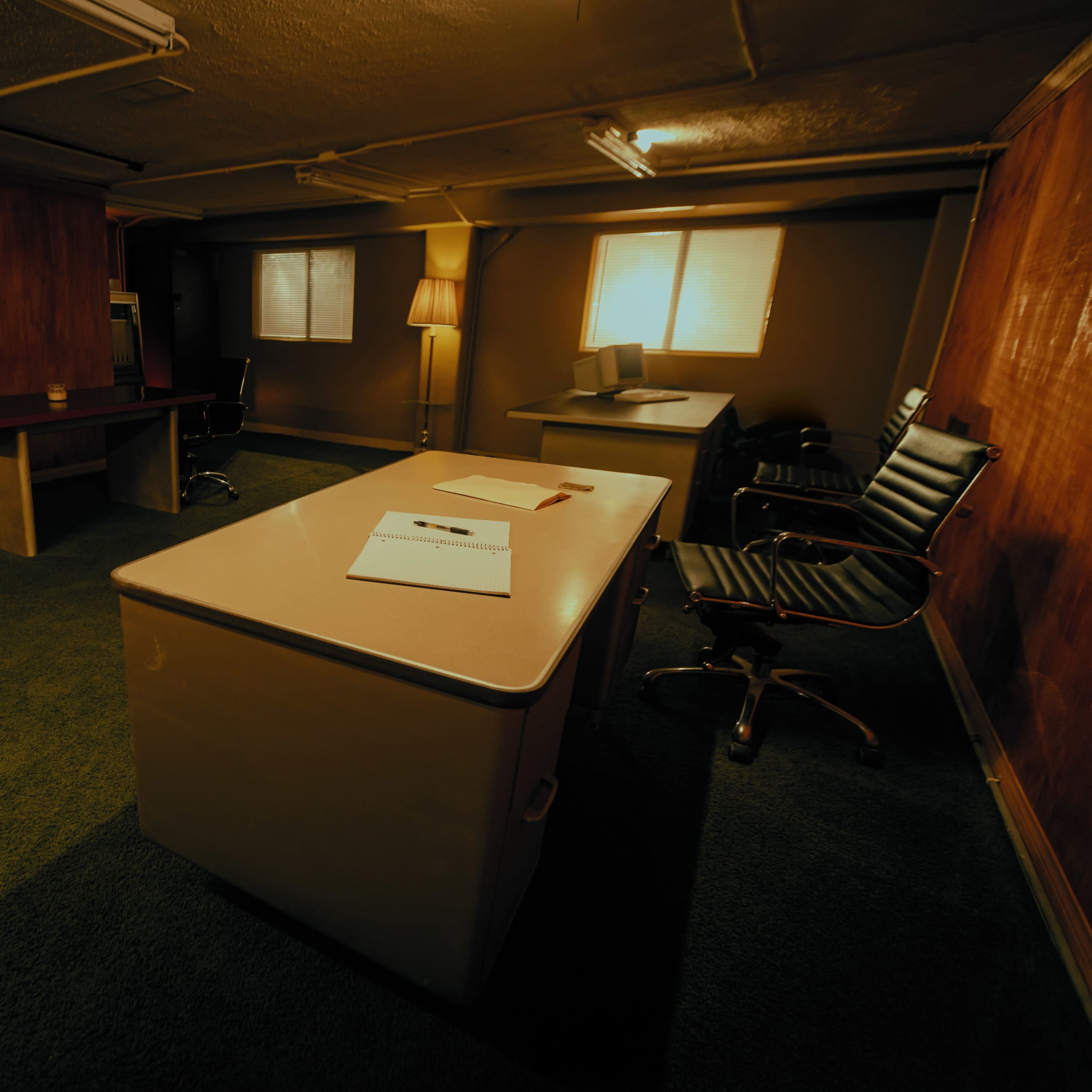 An empty office space features a desk, chairs, and a warm, low-lit atmosphere with wooden paneling.
