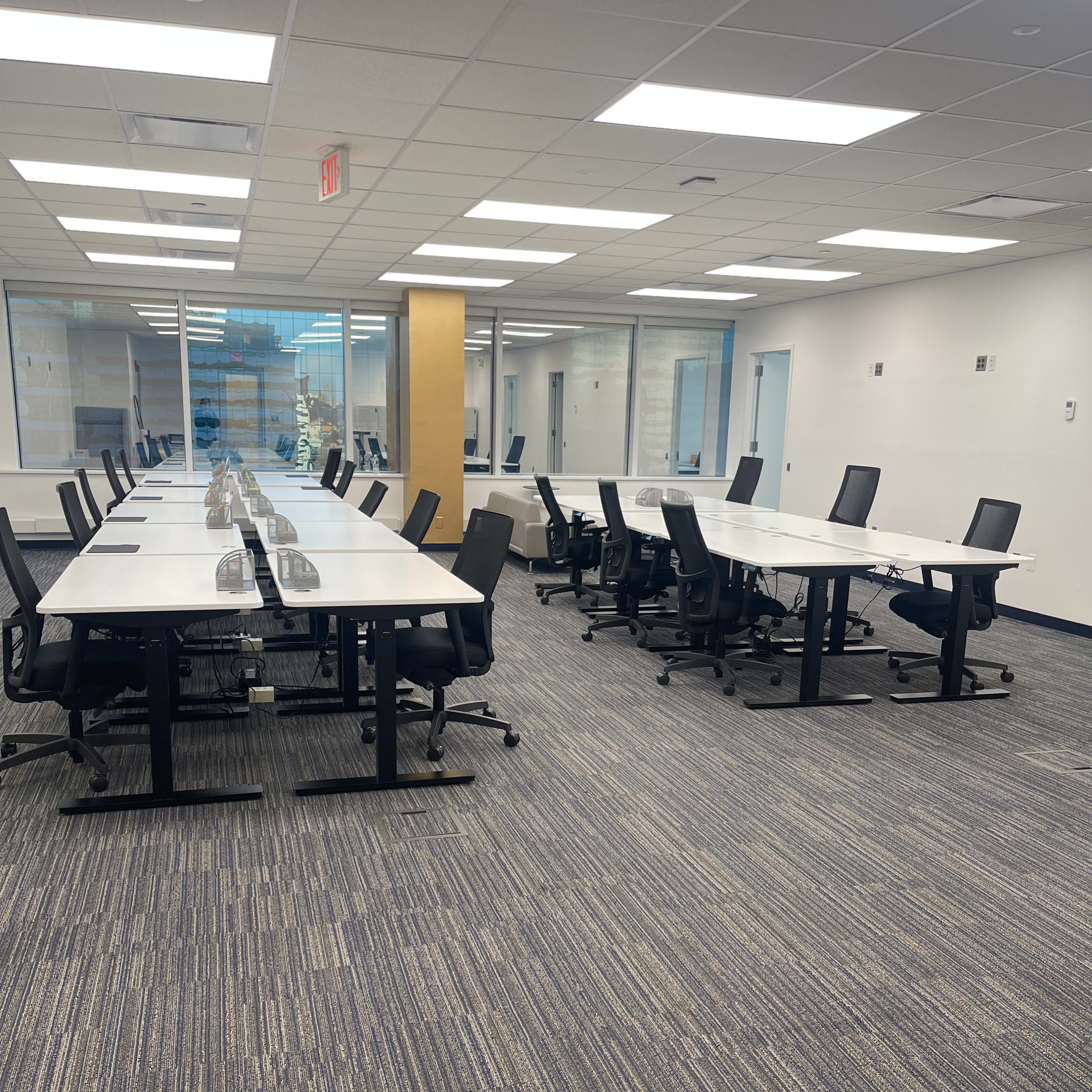 A large, empty office space with rows of desks and chairs arranged neatly along the floor.