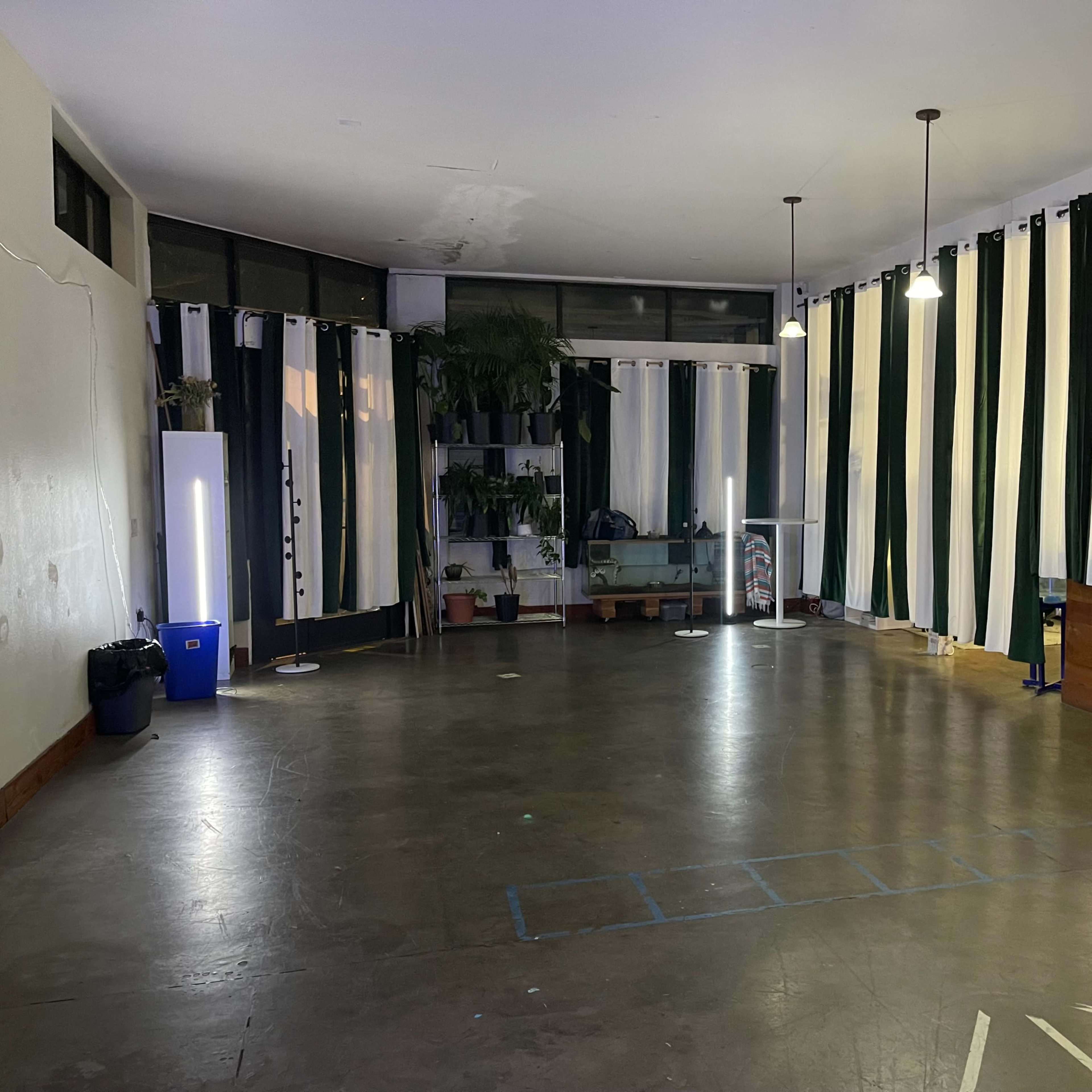 A spacious room with large windows, minimal furnishings, and tall curtains in green and white.