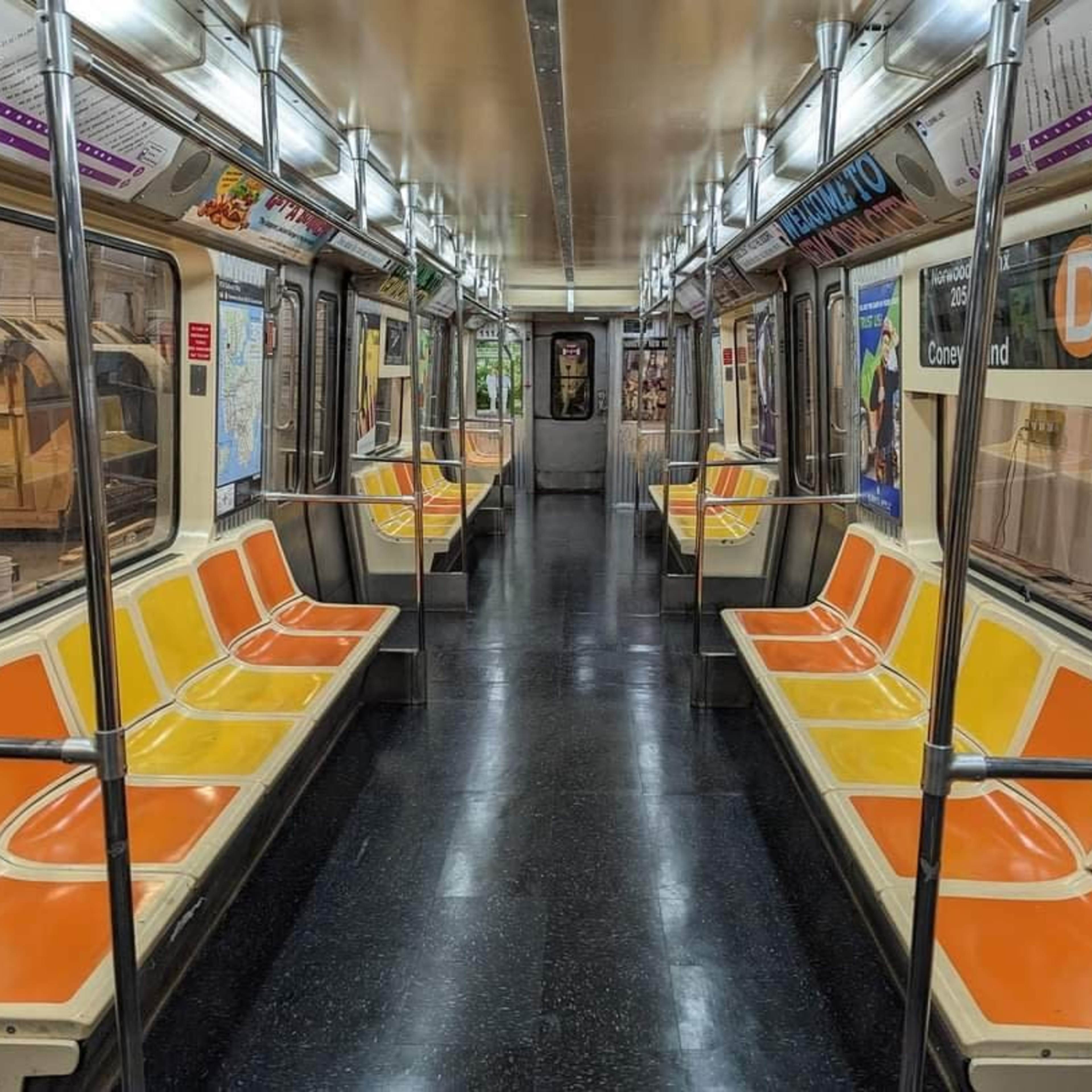 An empty subway train interior with orange and yellow bench seating, glossy black flooring, and advertisements on the walls.