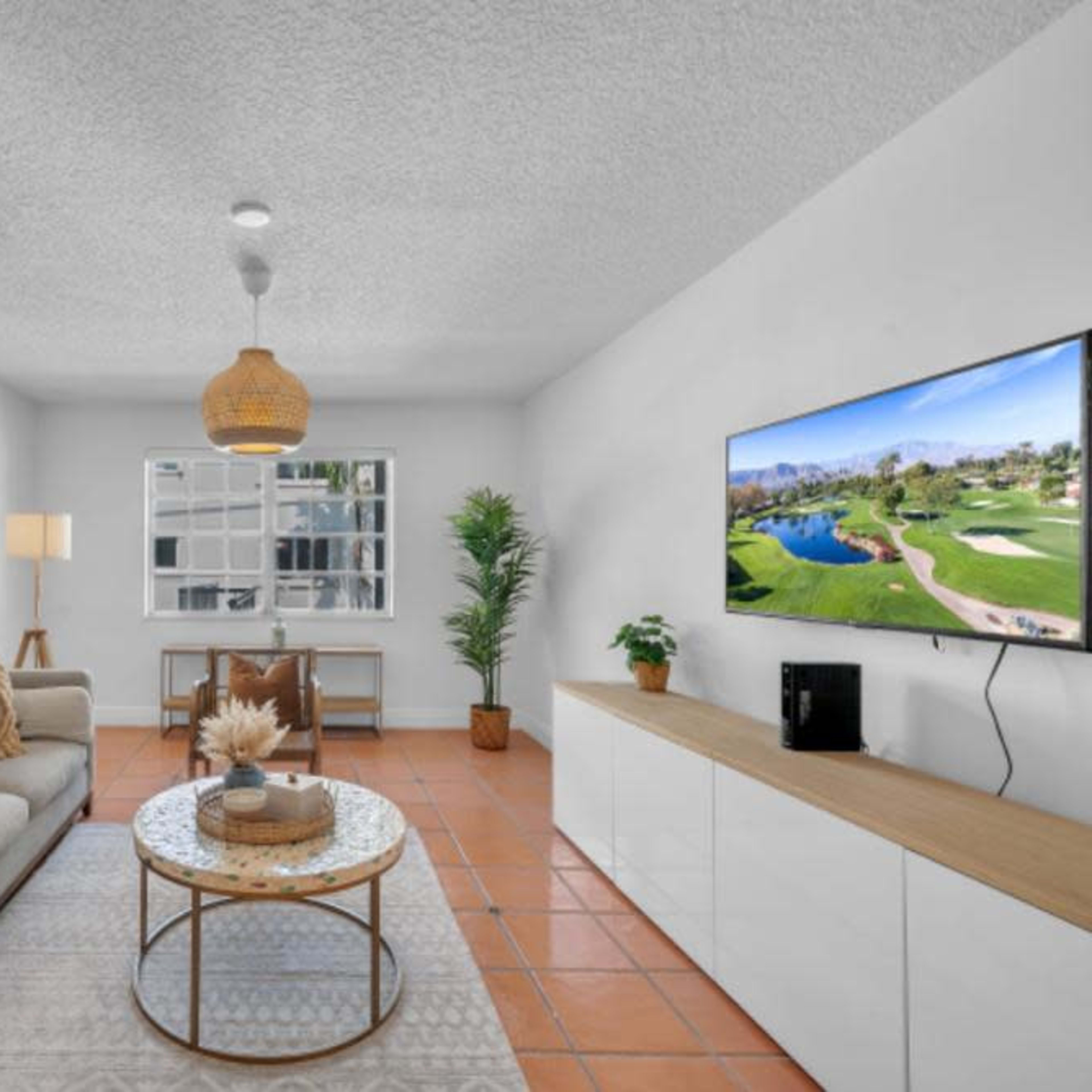 A modern living room with a beige sofa, a round coffee table, a television mounted on the wall, and decorative elements like plants and framed art.