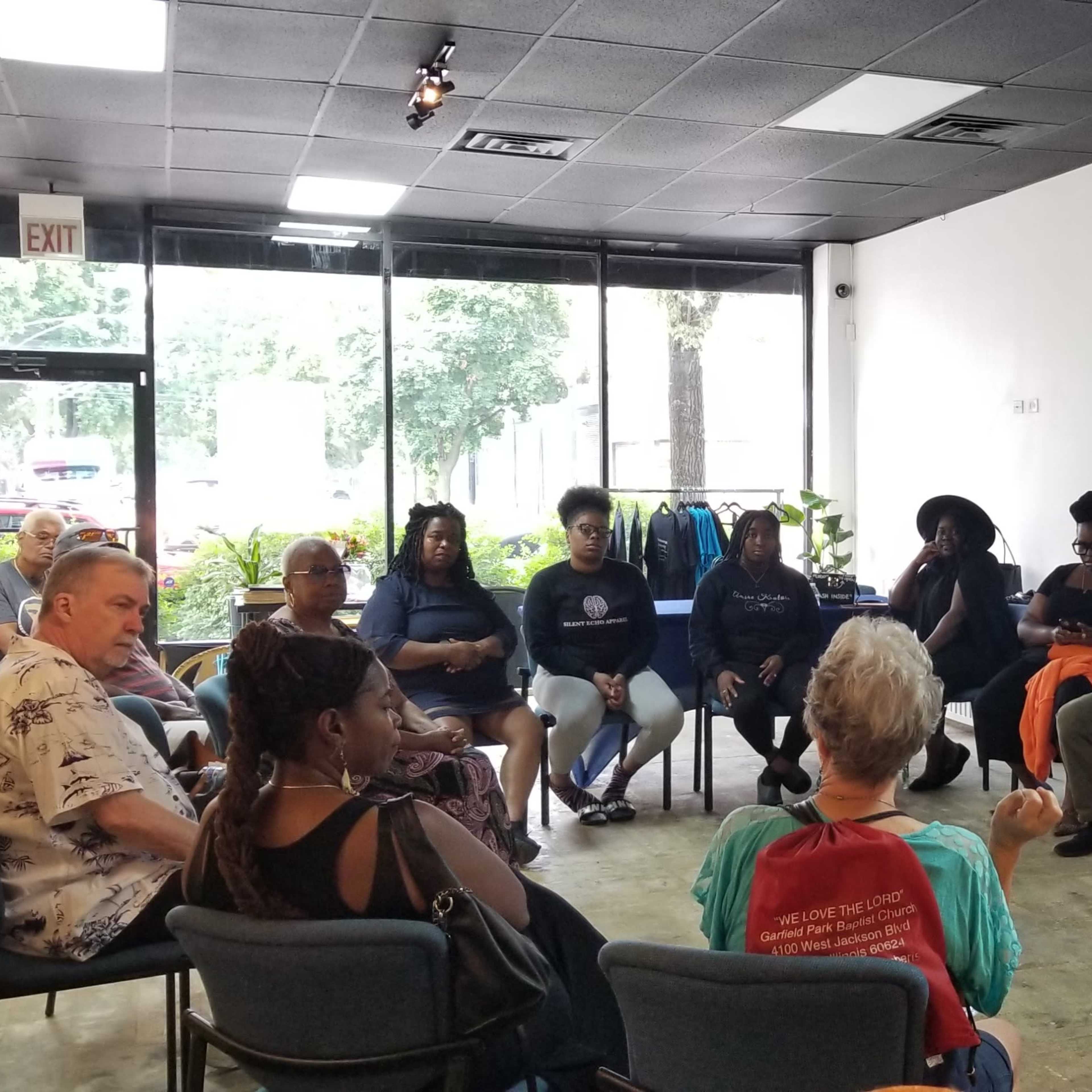A group of people sits in a circle in a well-lit room with artwork displayed on the wall.