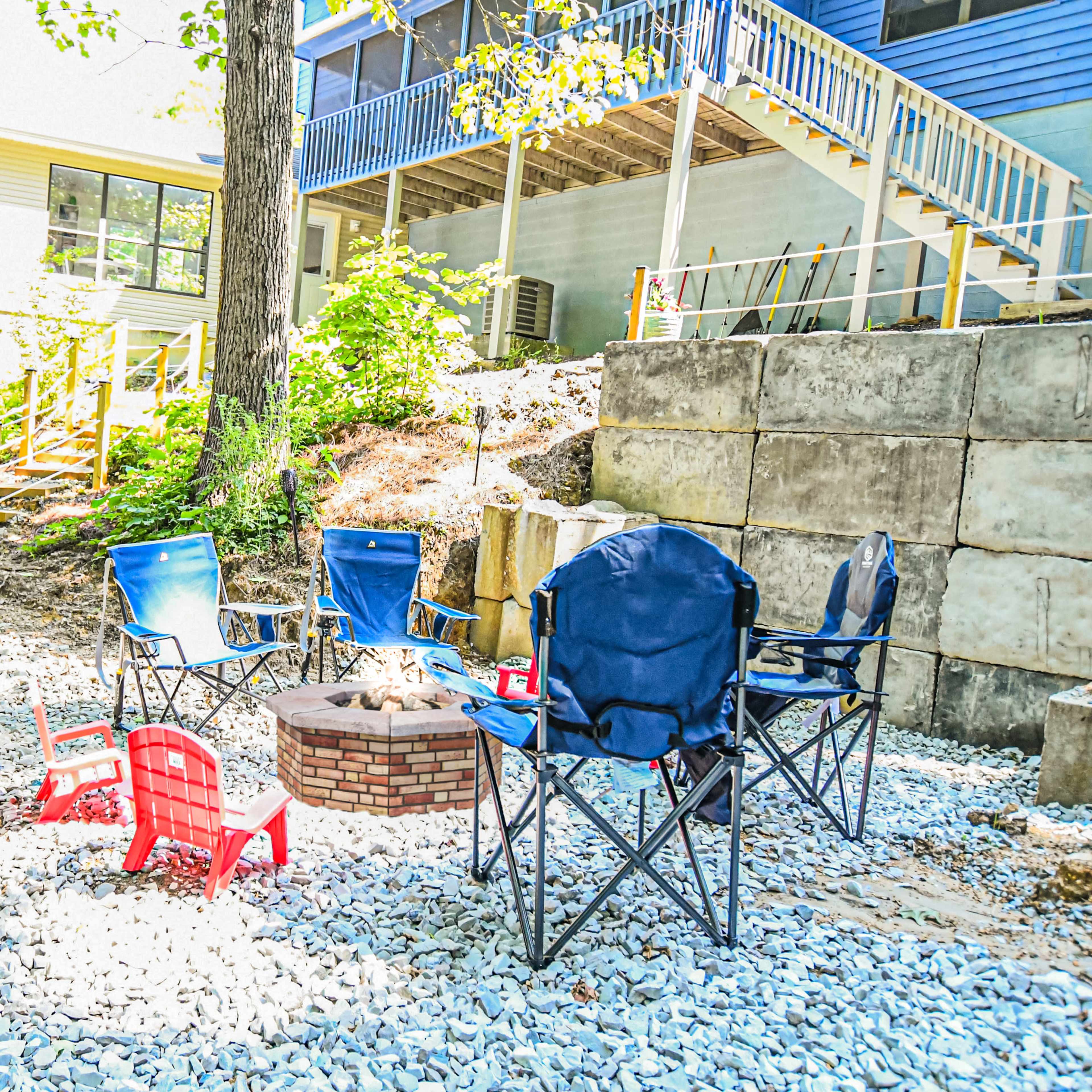A circle of chairs surrounds a fire pit in a gravel area next to a house with a blue exterior.