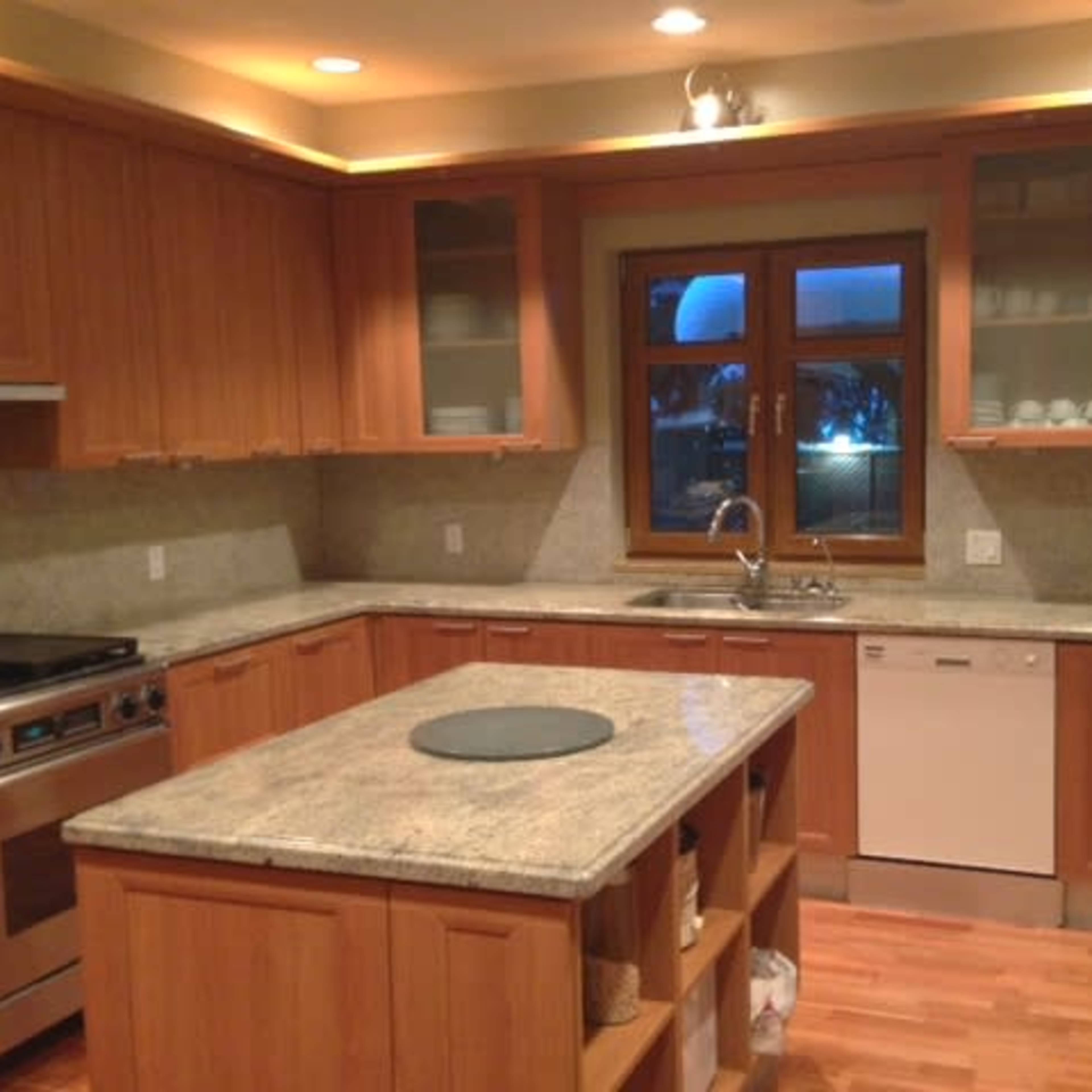 A modern kitchen with wooden cabinetry, granite countertops, and stainless steel appliances, including a dishwasher and a gas stove.