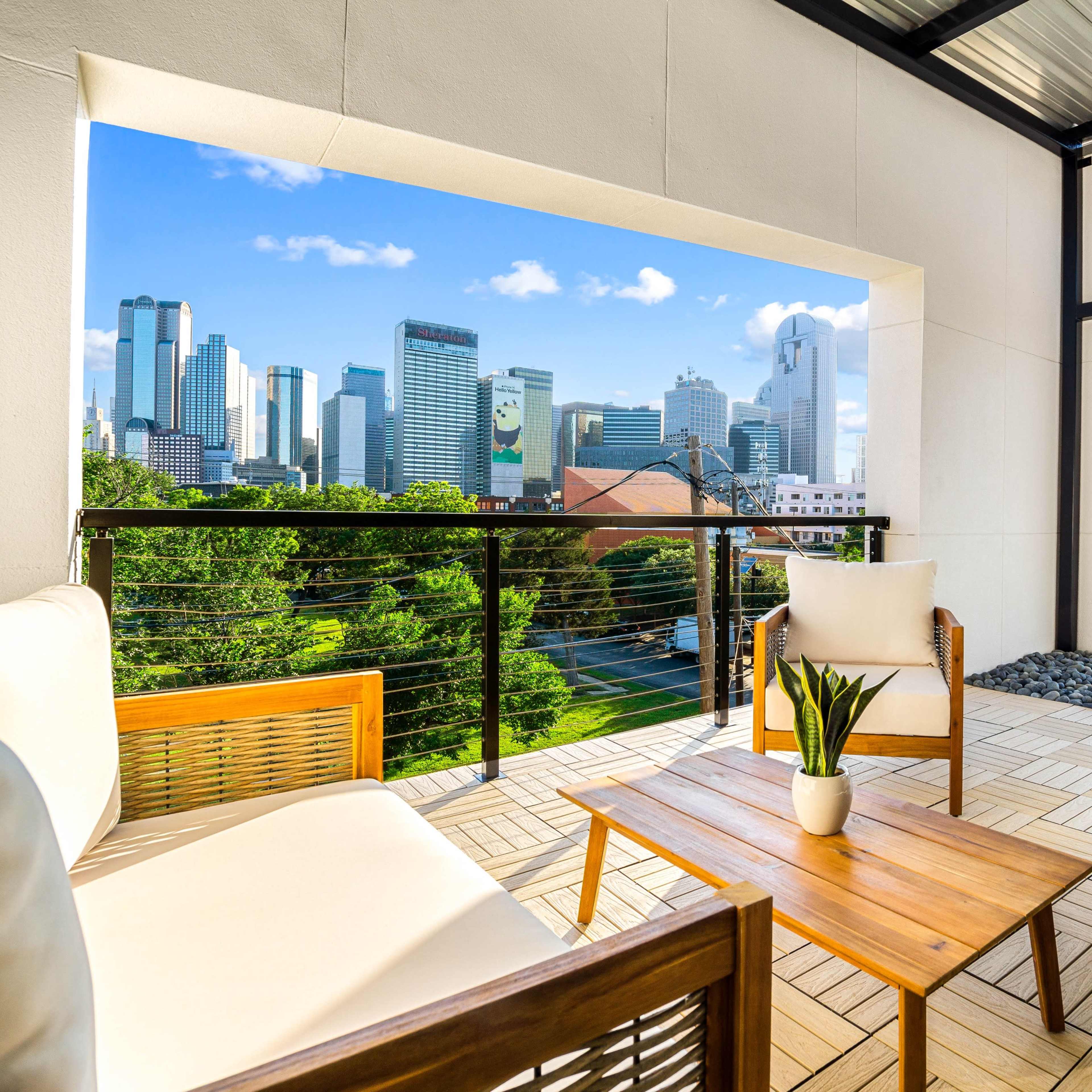 A modern balcony with two chairs and a table, overlooking a city skyline filled with tall skyscrapers.