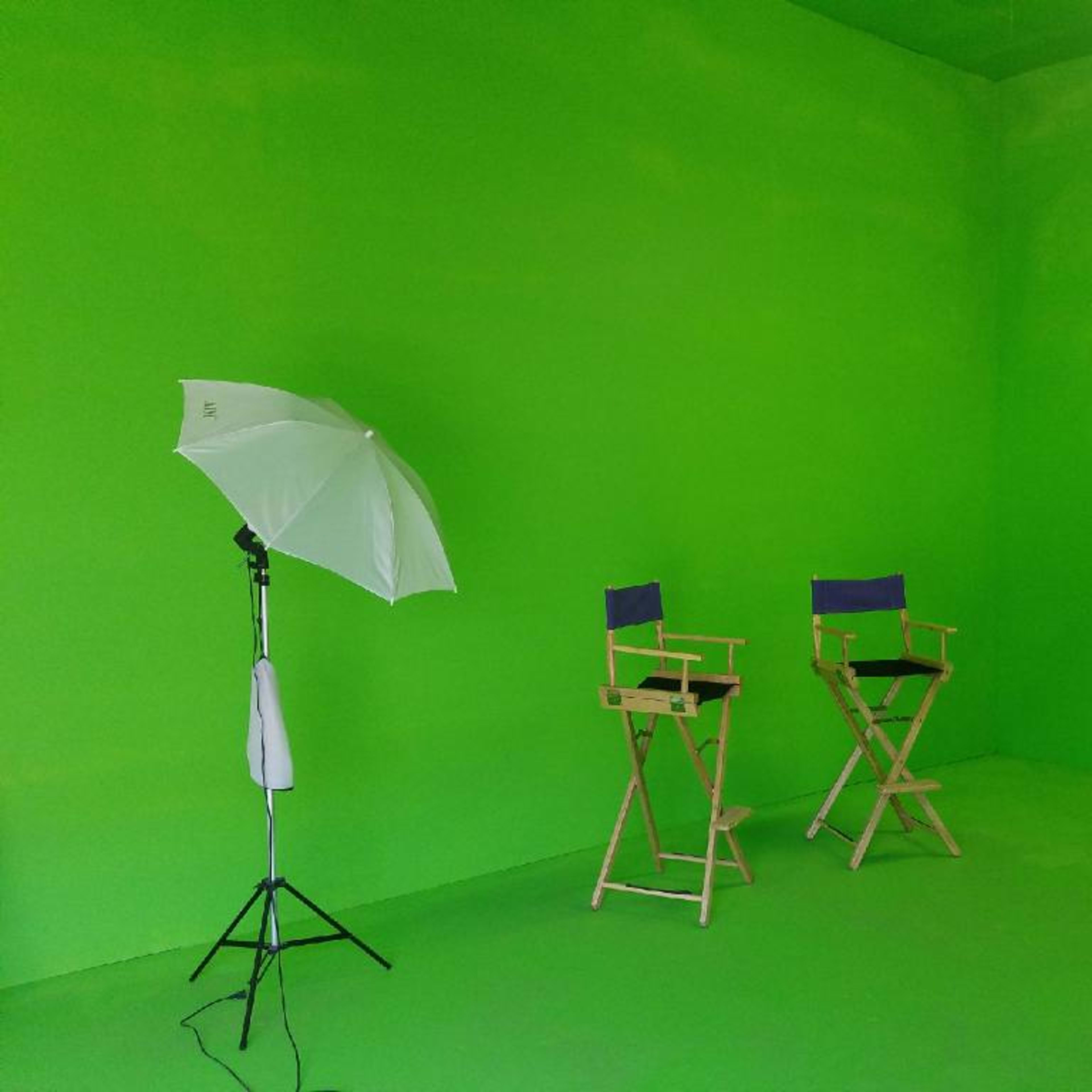 A blank green room with two director's chairs and a lighting umbrella.