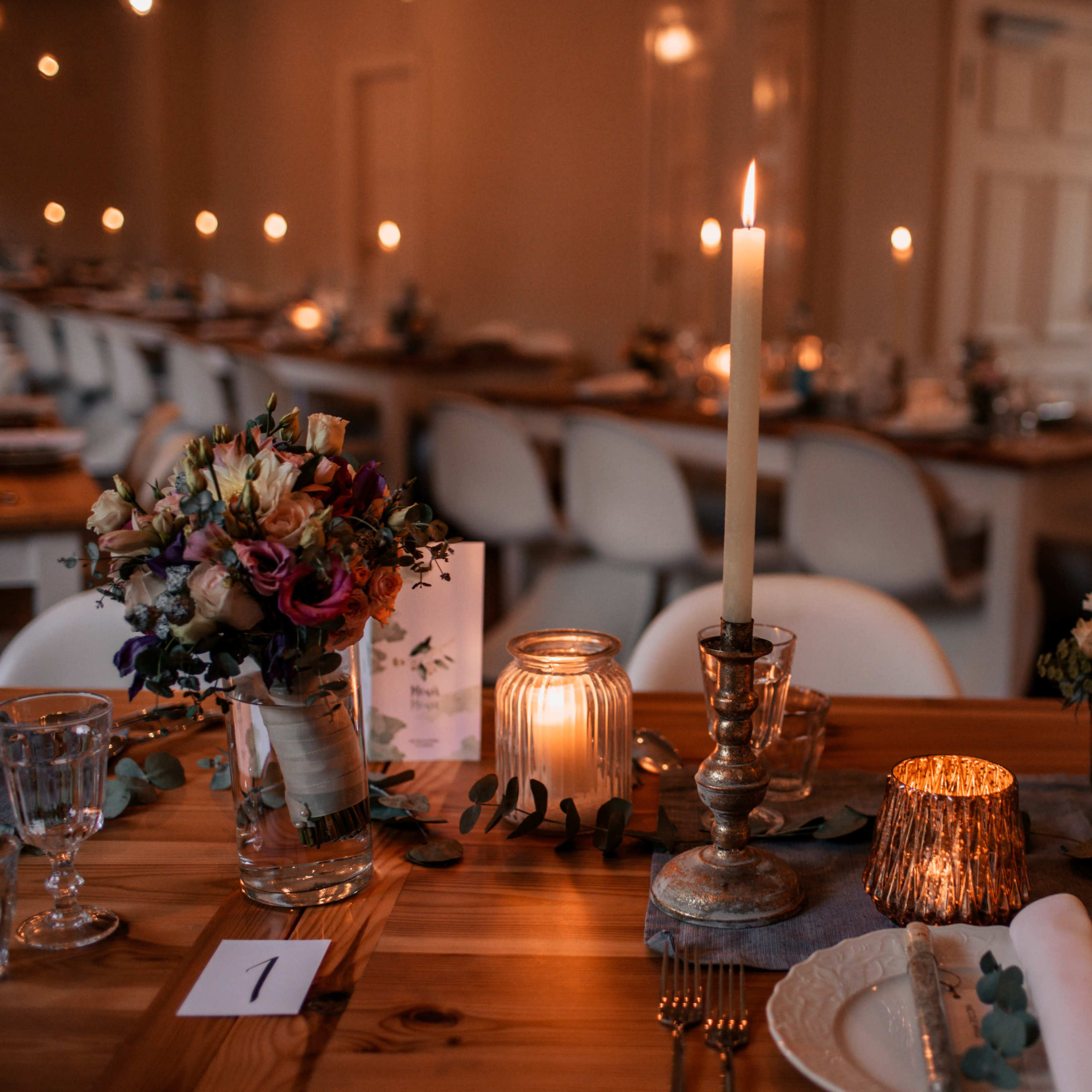 A beautifully arranged dining table set for an event, featuring floral centerpieces, candles, and elegant tableware.