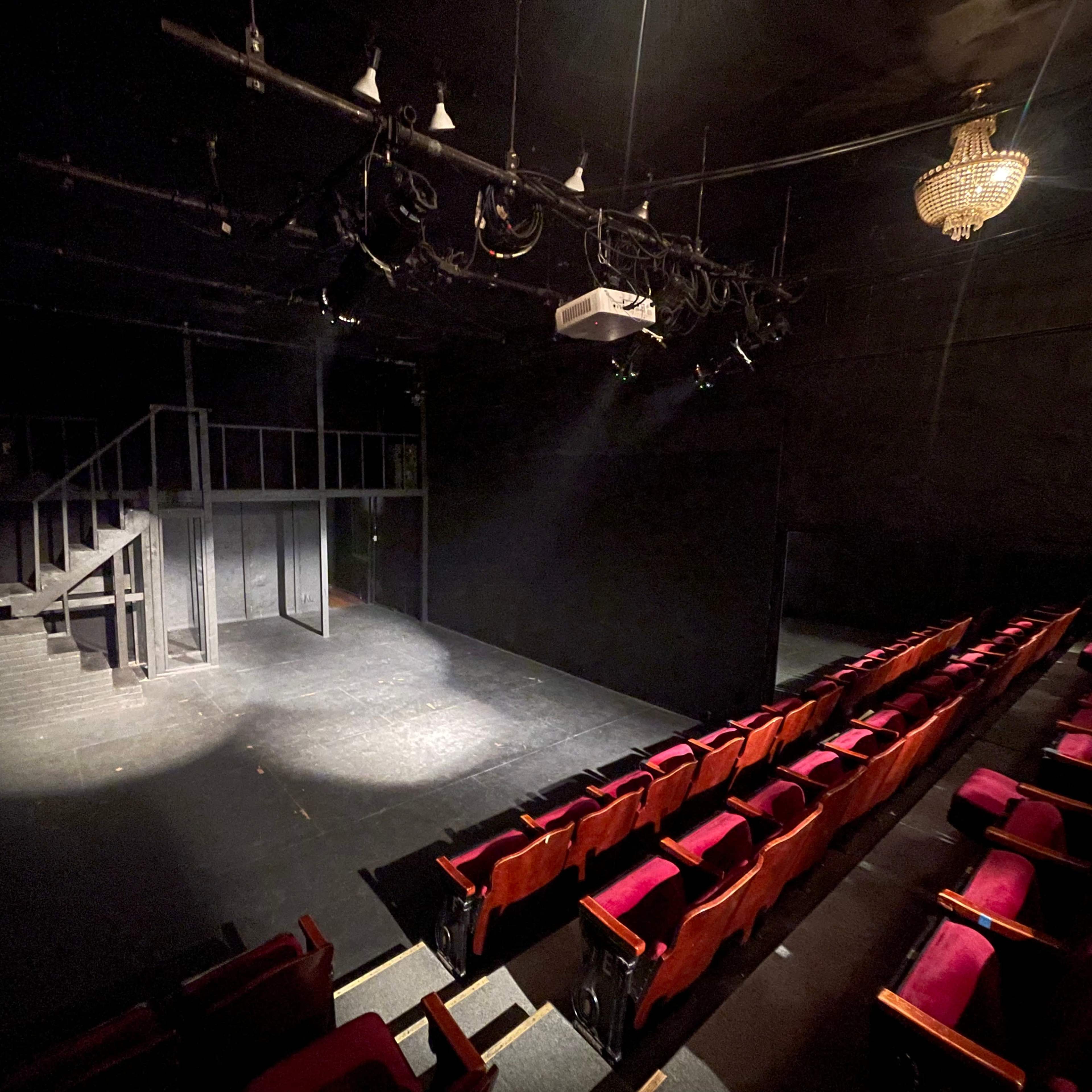 A dimly lit theater with red seats facing a stage that includes a raised platform and a staircase.