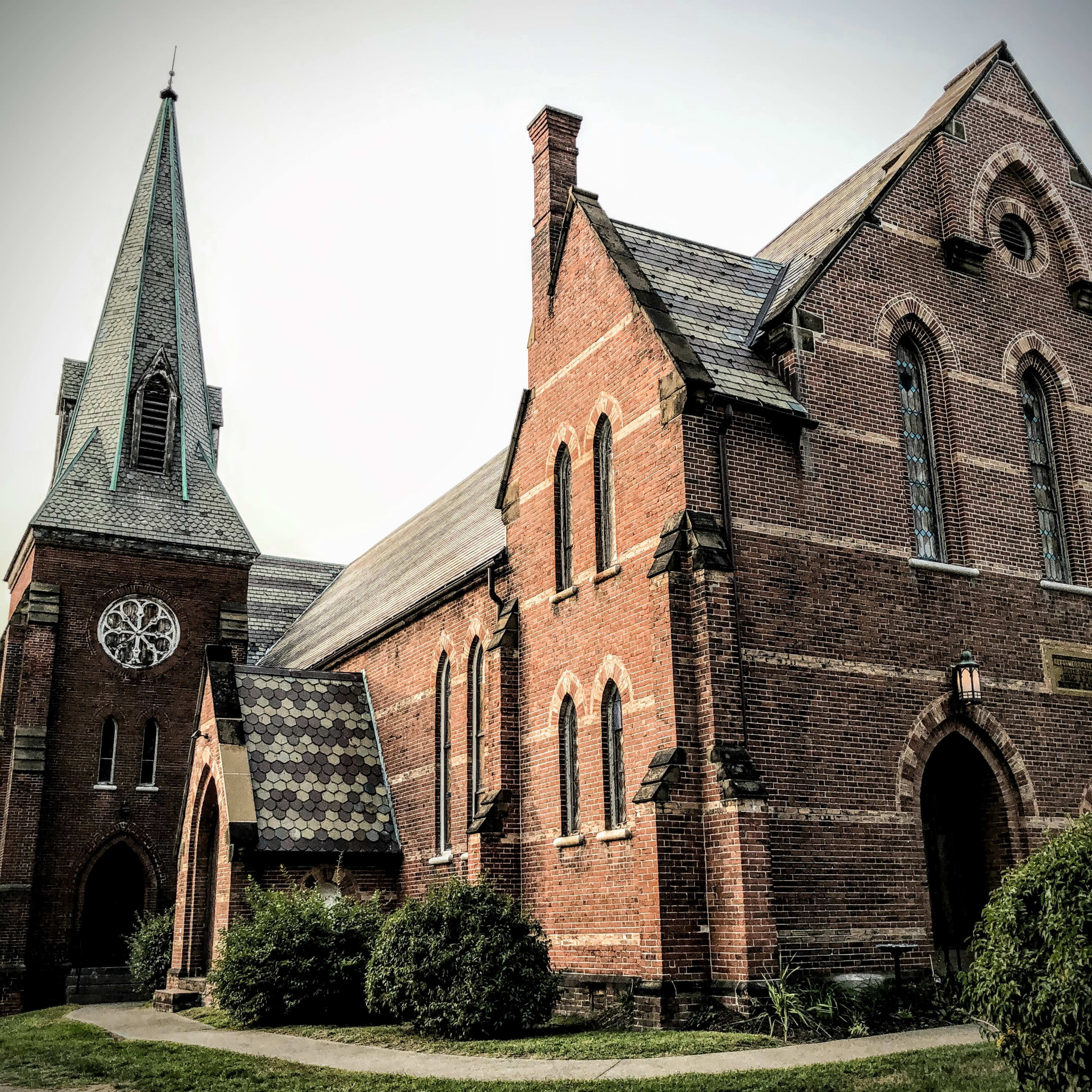 A historic brick church with a tall steeple and stained glass windows.