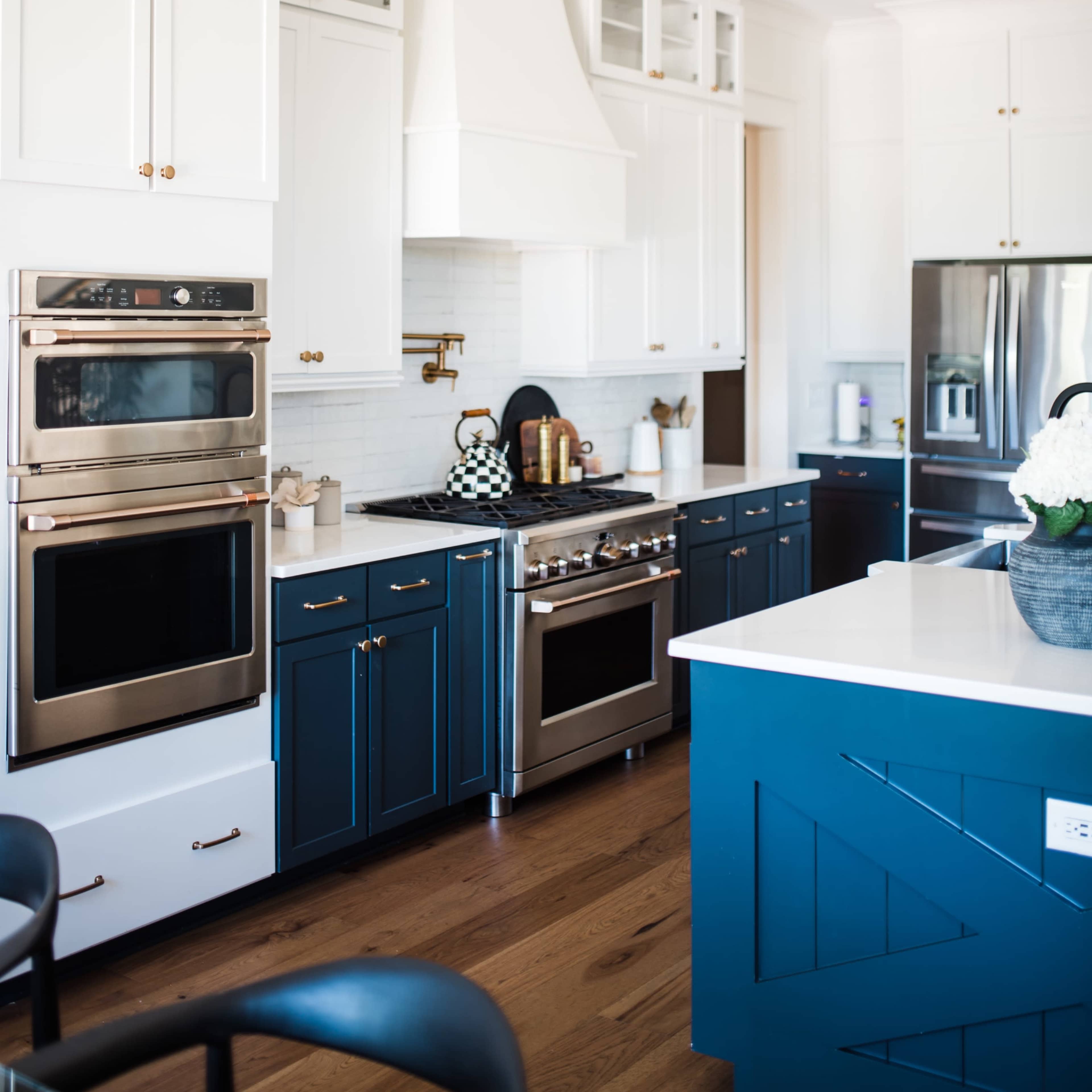 A modern kitchen featuring white upper cabinets, navy blue lower cabinets, stainless steel appliances, and a large island with a countertop.