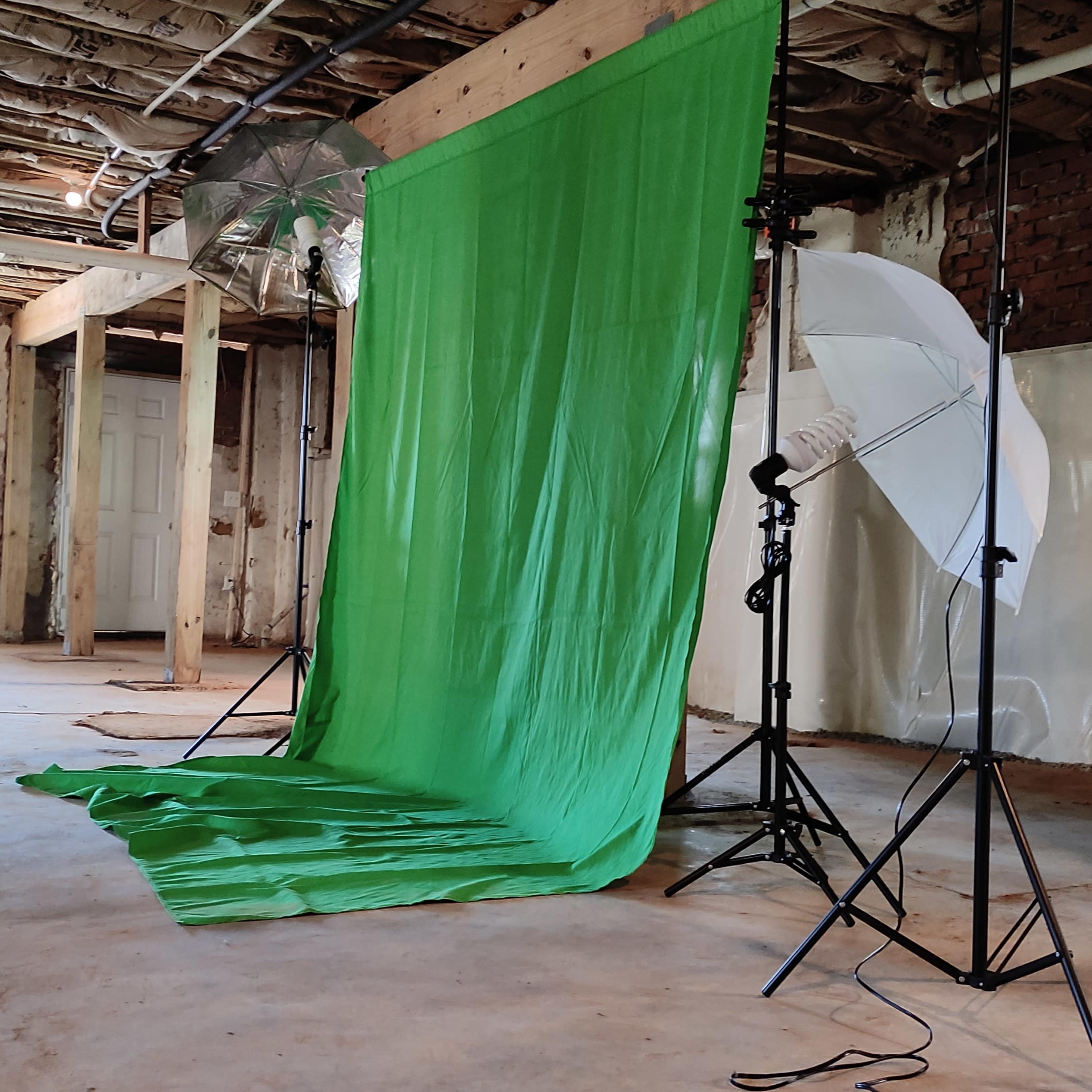 A spacious, unfinished room with a green backdrop setup for photography, accompanied by lighting equipment on stands.
