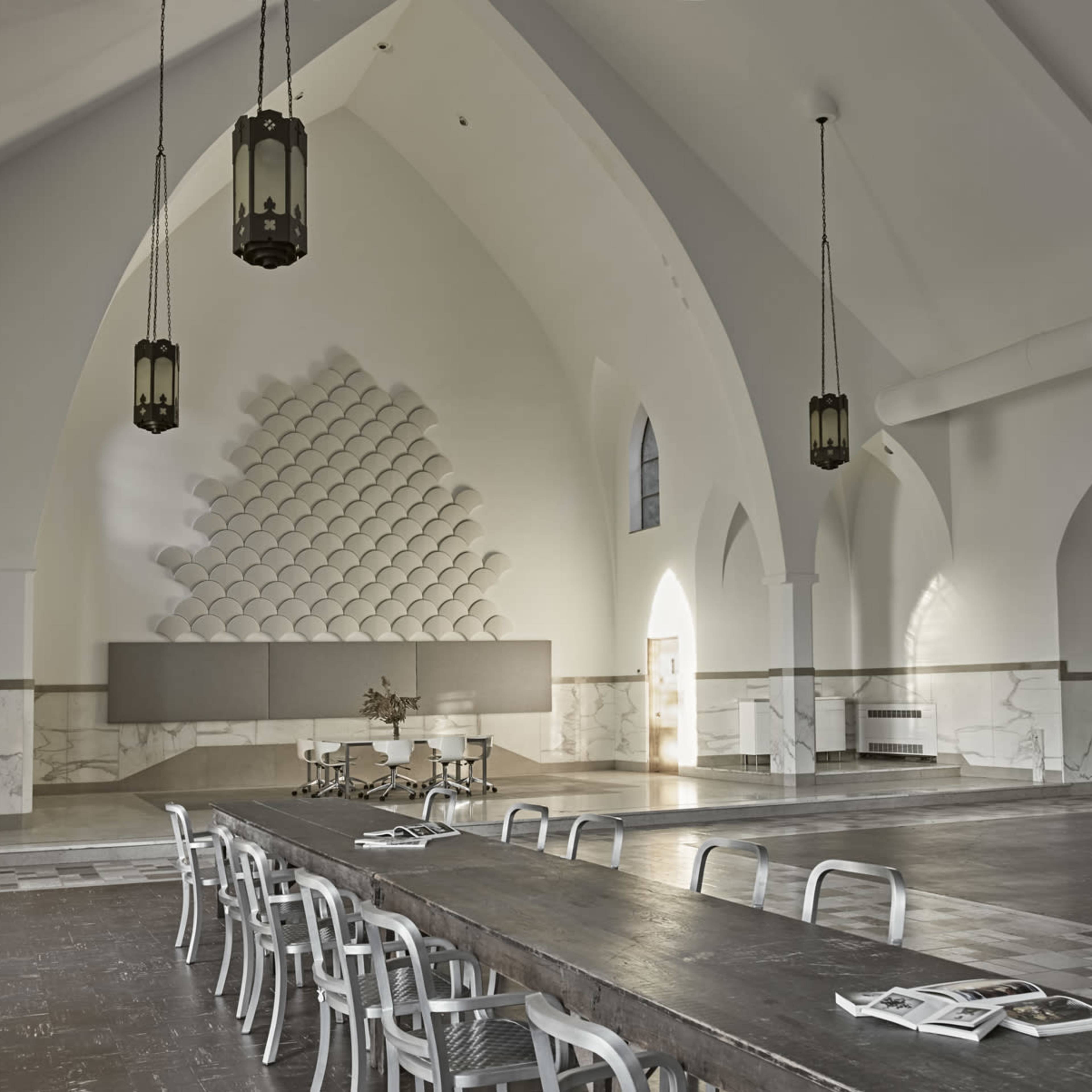 A spacious interior with high arched ceilings, a long wooden table, and minimalist furniture arranged in a bright, airy room.